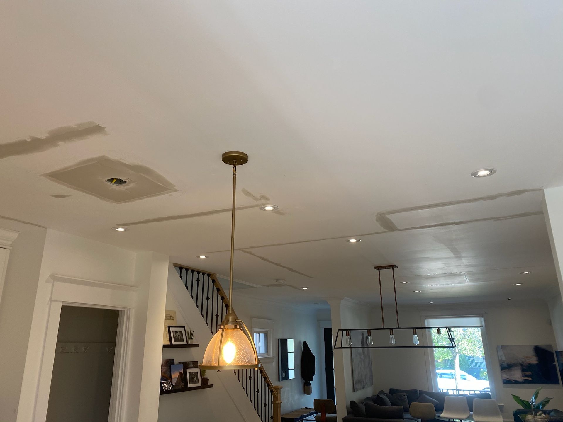 Interior view of a ceiling with recessed lighting and a hanging pendant lamp, open to a staircase and living area.