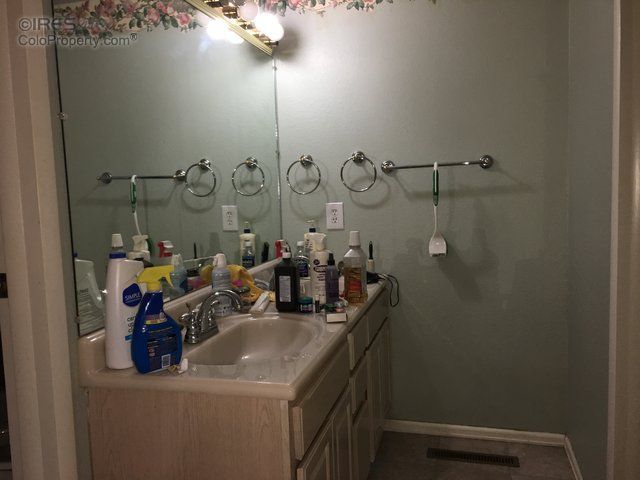 Bathroom vanity with a sink, mirror, and toiletries; towels hang on wall hooks.