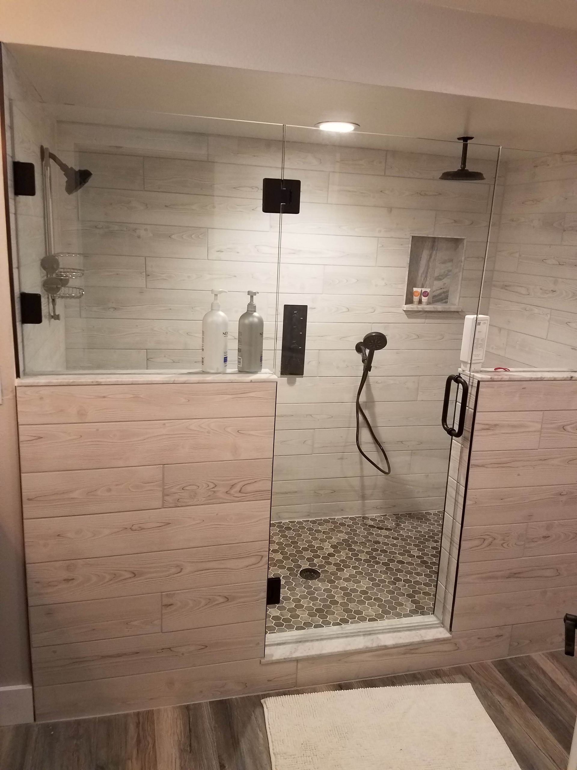 Modern walk-in shower with beige tile, glass door, pebble floor, and black fixtures.