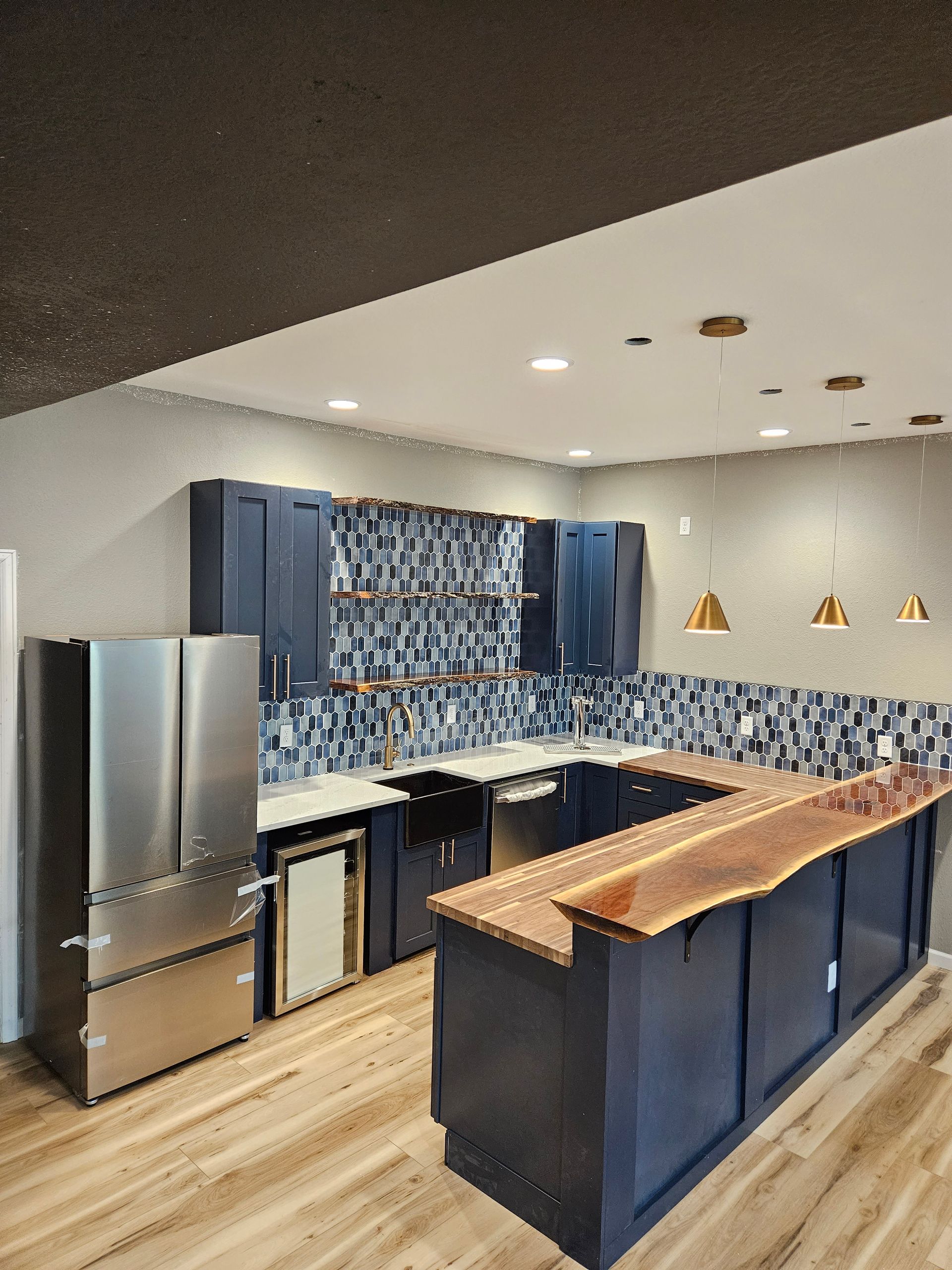 Modern kitchen with blue cabinets, stainless fridge, patterned backsplash, and wood island counter.