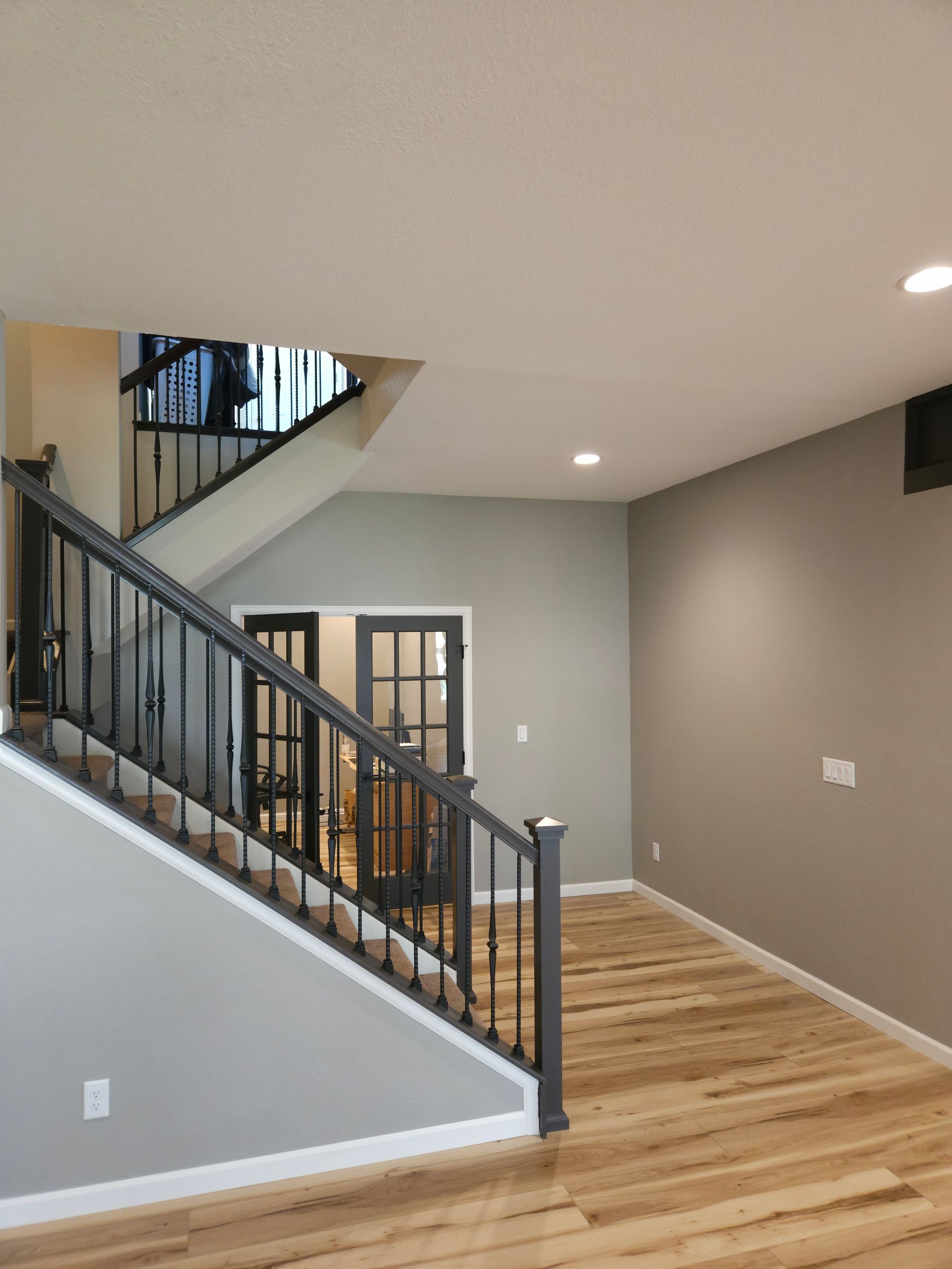 Staircase and open living area with gray walls, wood floors, and dark railing.