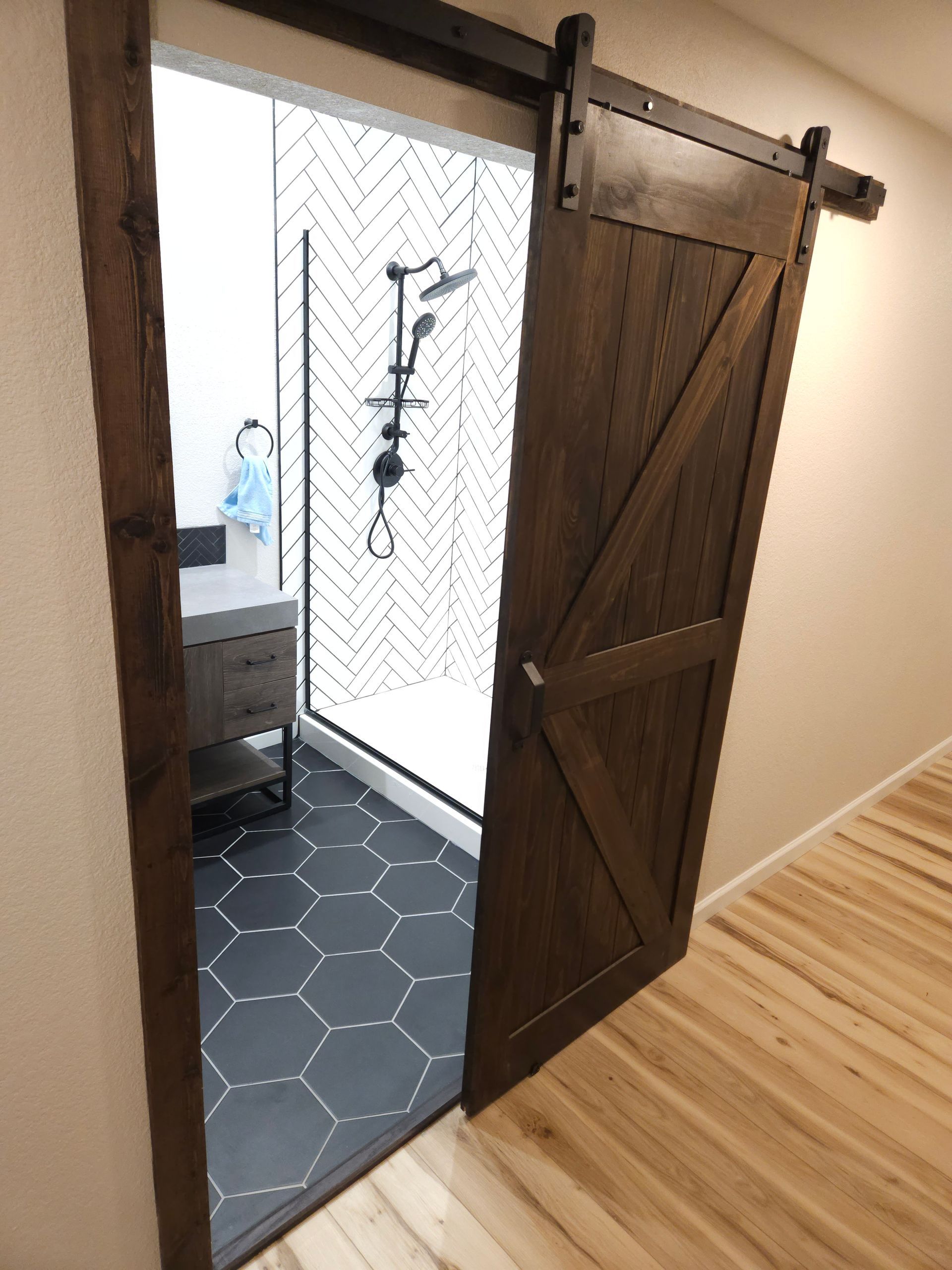 Open wooden barn door to a tiled bathroom with patterned floor and shower fixture visible.