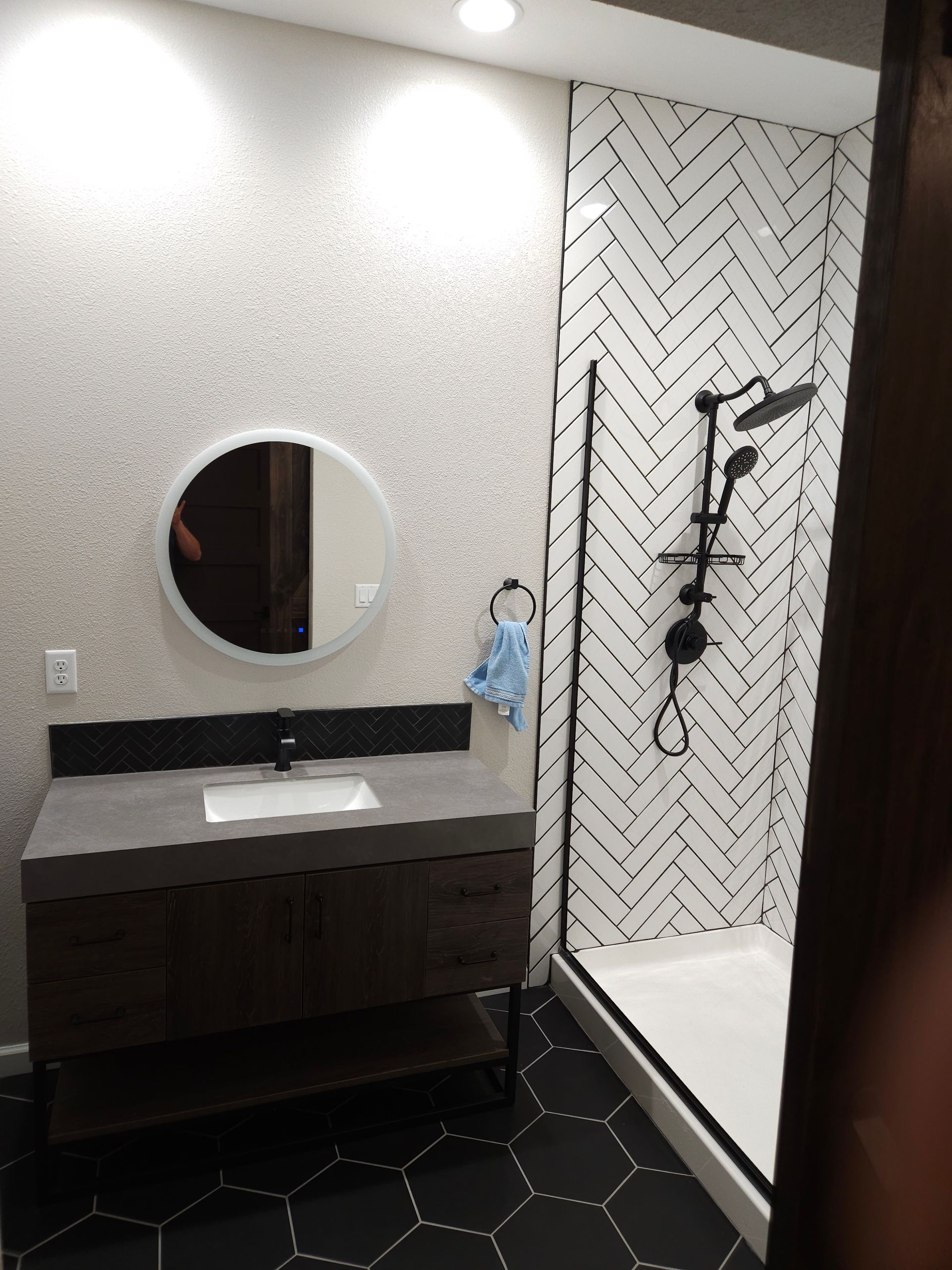 Modern bathroom with dark vanity, round mirror, and black-and-white tiled shower.