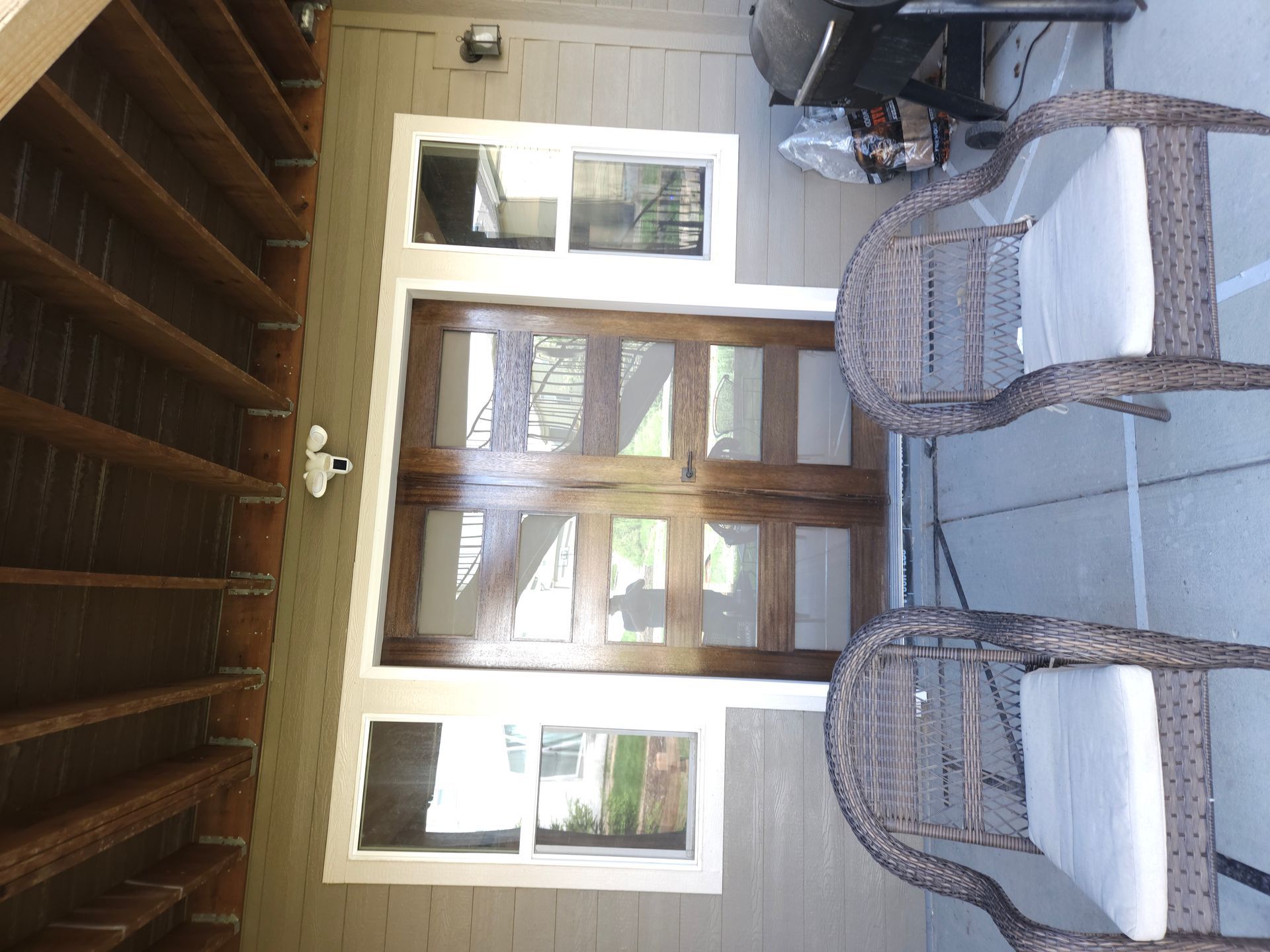 Patio with wicker chairs, glass-top table, and wooden doors beside a covered porch