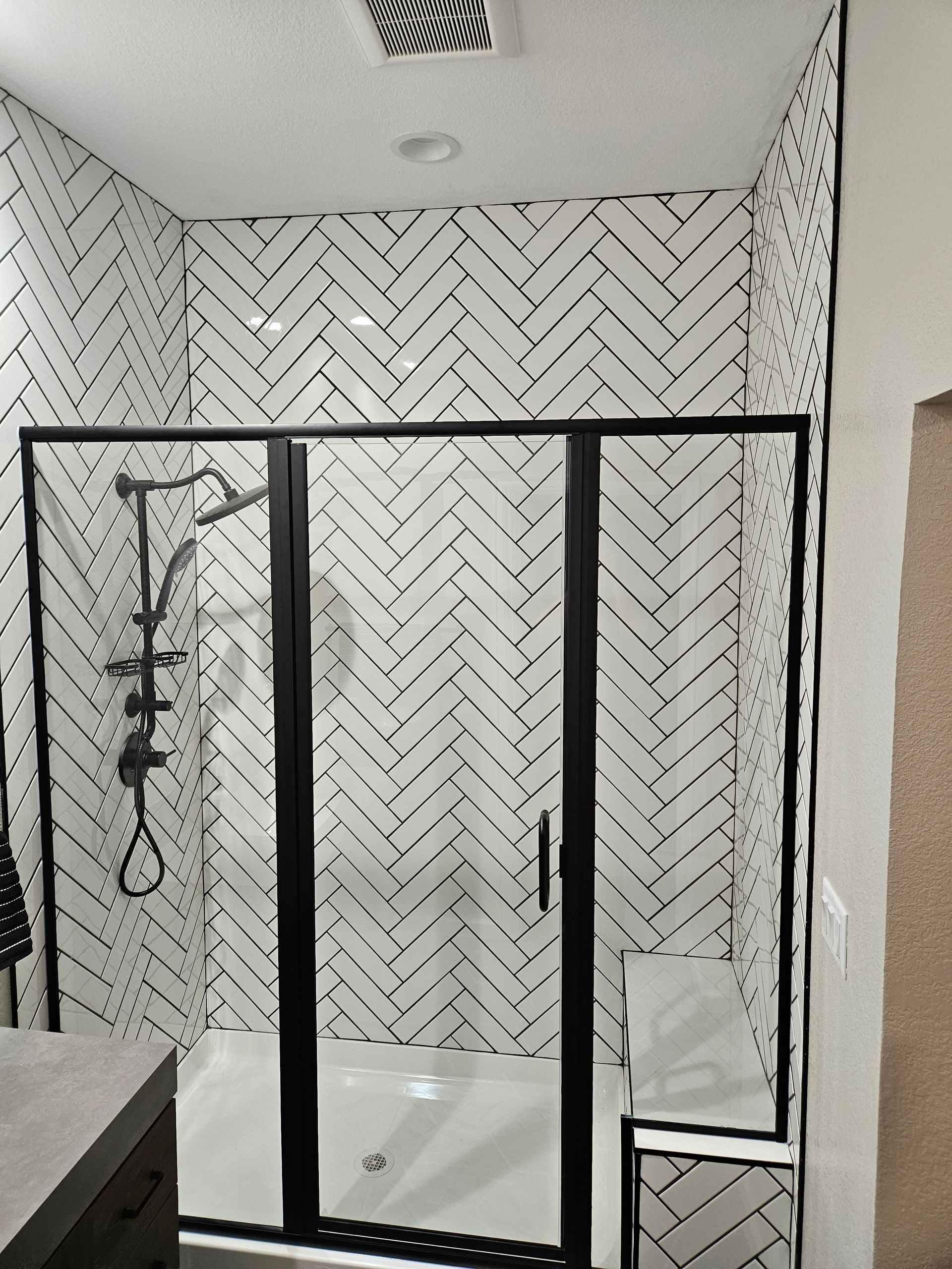 Black-framed shower enclosure with herringbone tile walls in a bathroom.