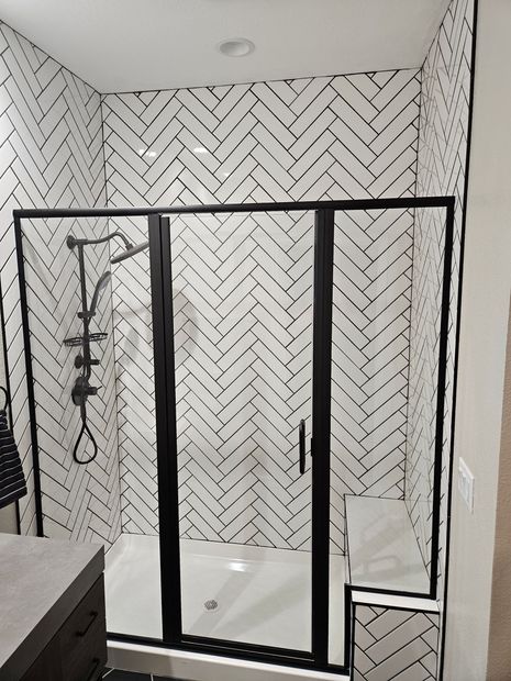 Black-framed glass shower enclosure in a herringbone-tiled bathroom