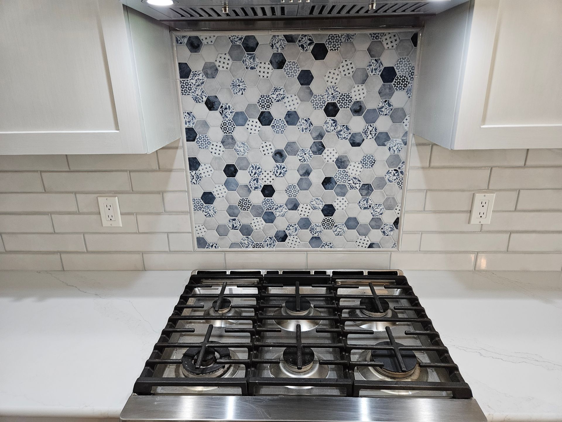 Modern kitchen stove with white cabinets, gray tile backsplash, and blue floral accent tile behind the cooktop