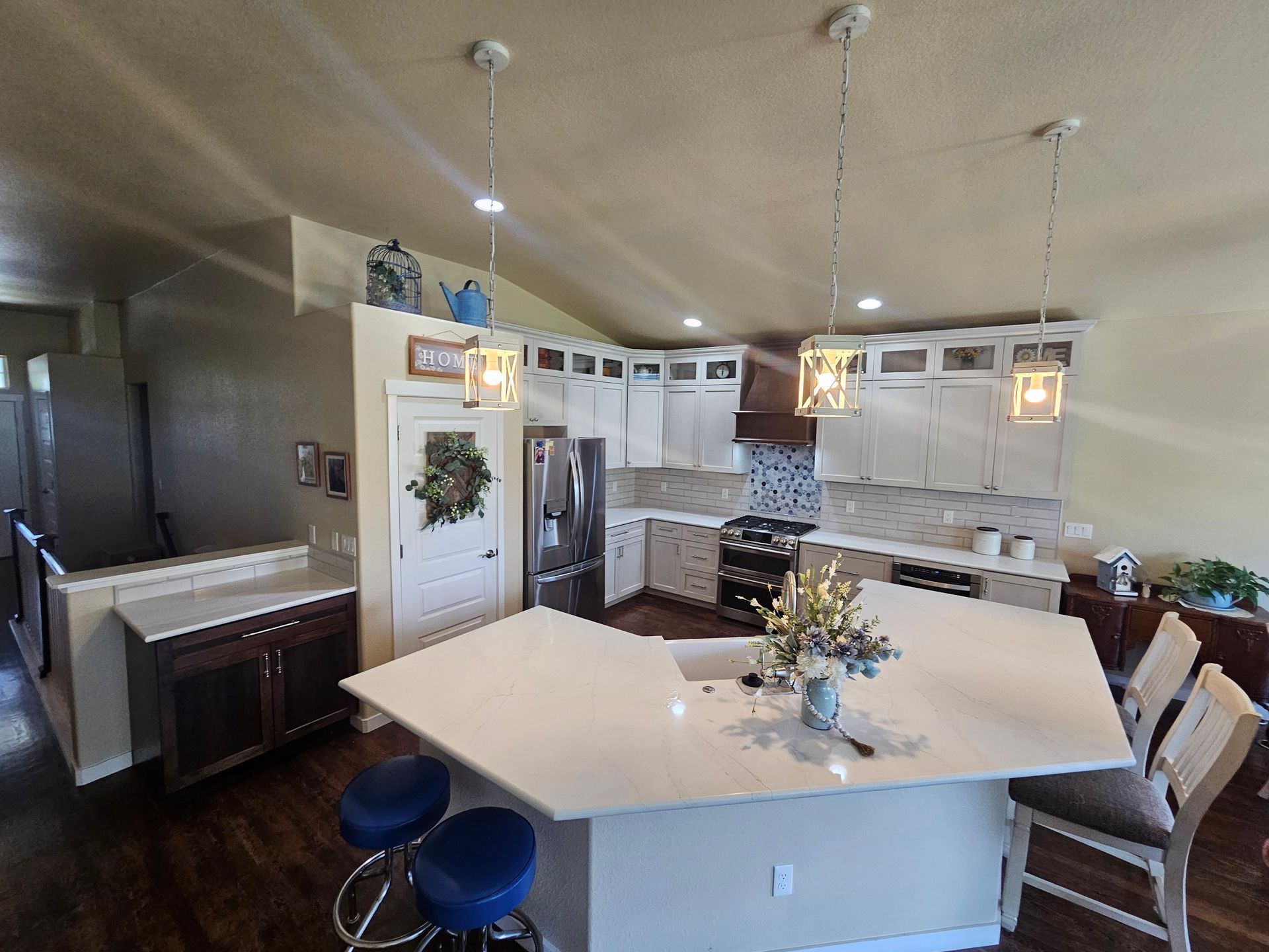 Modern kitchen with white island, hanging lights, bar stools, and stainless appliances
