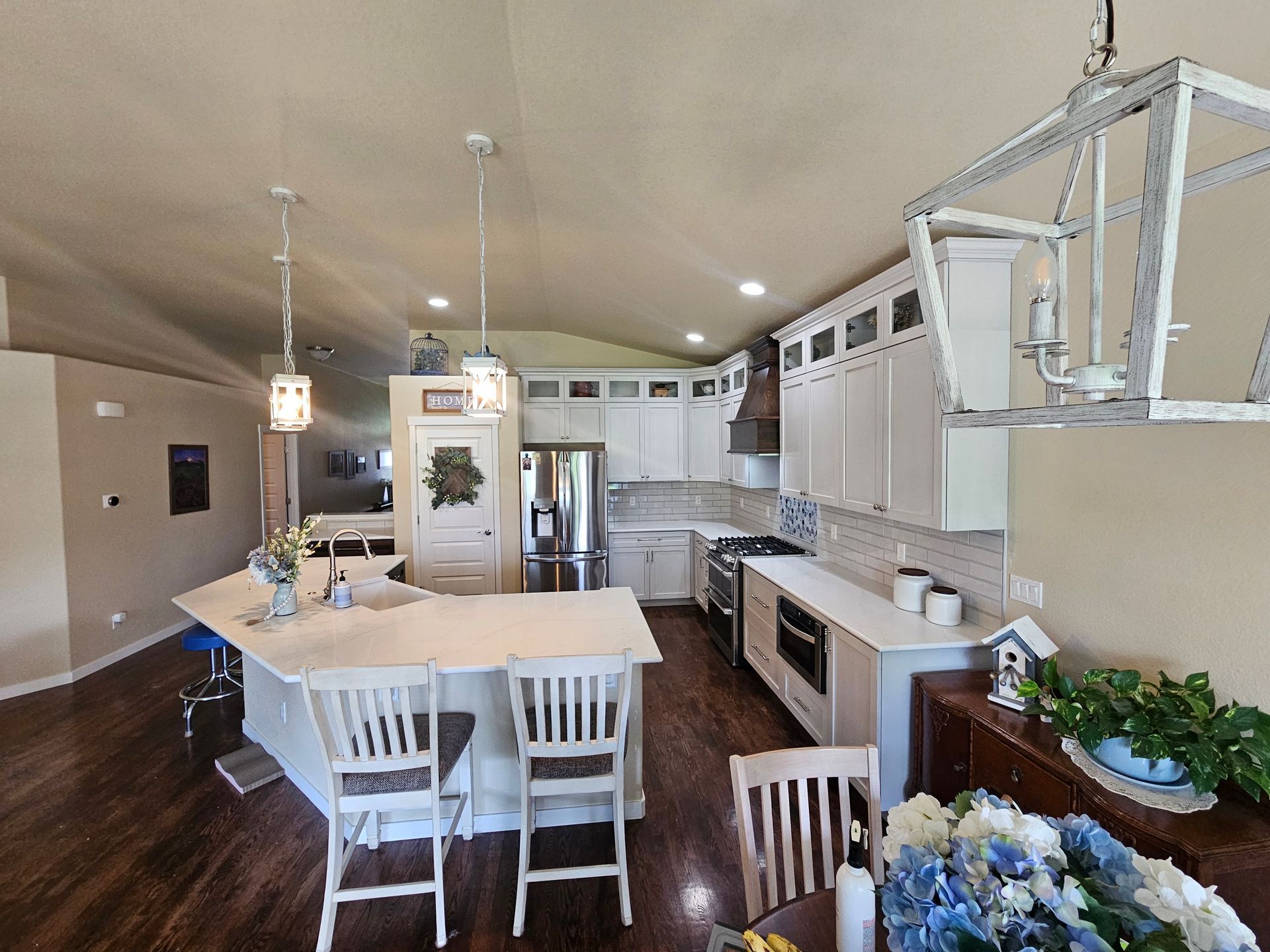 Bright, modern kitchen with white cabinets, island seating, pendant lights, and stainless steel appliances.