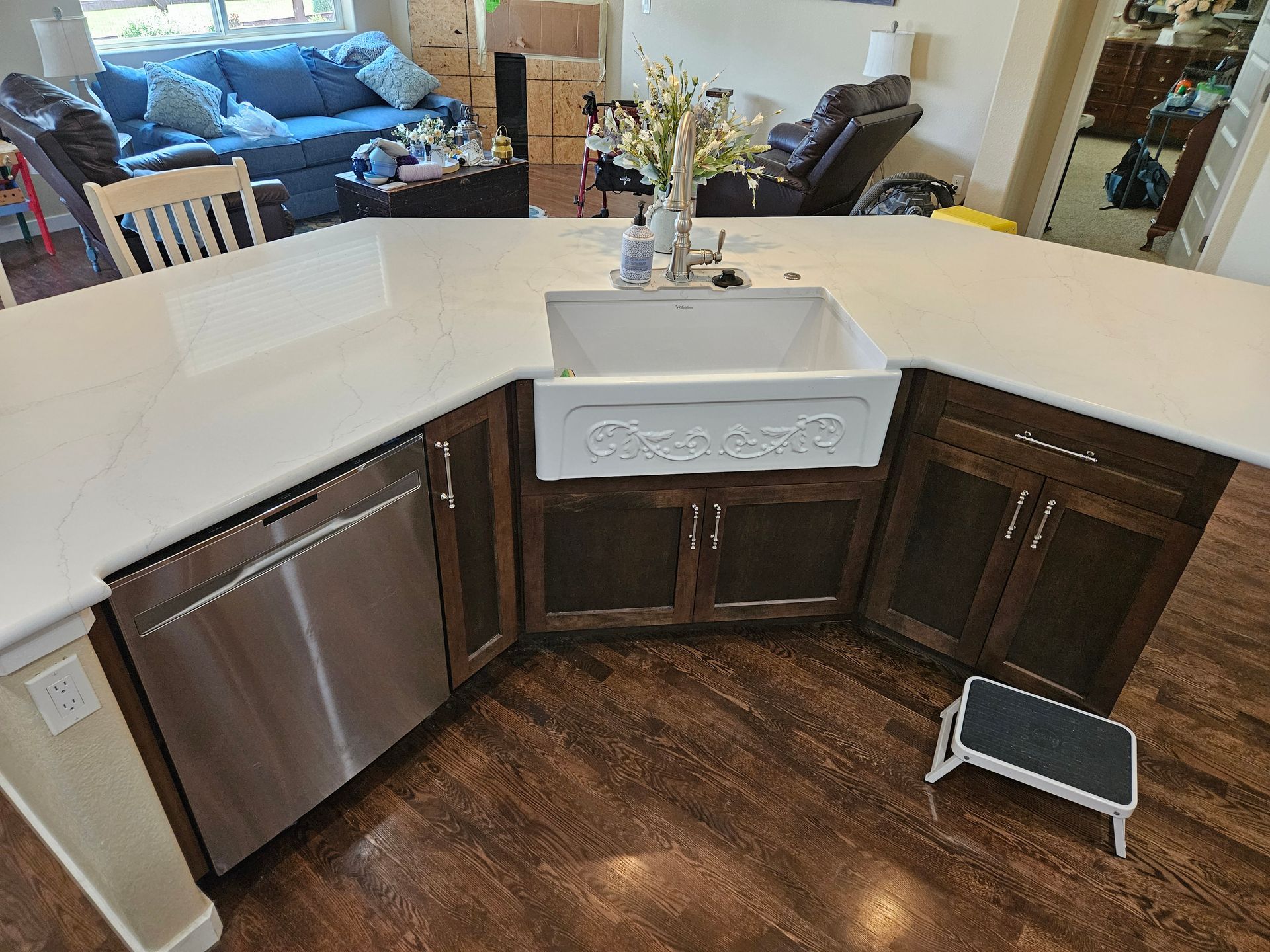 Kitchen with white countertop, stainless dishwasher, dark cabinets, and a small step stool on the floor.