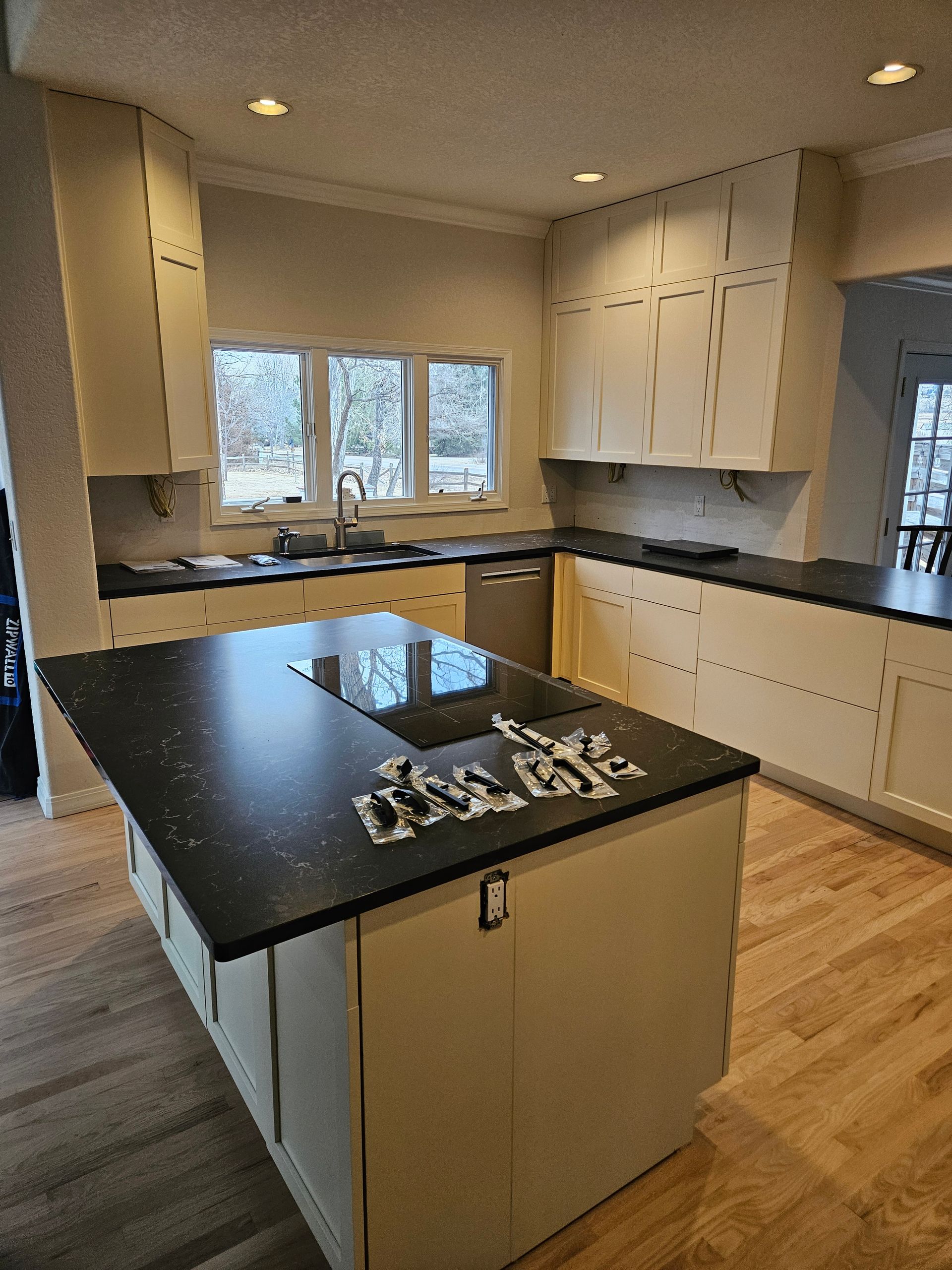 Modern kitchen with black island, white cabinets, wood floors, and large window above the sink