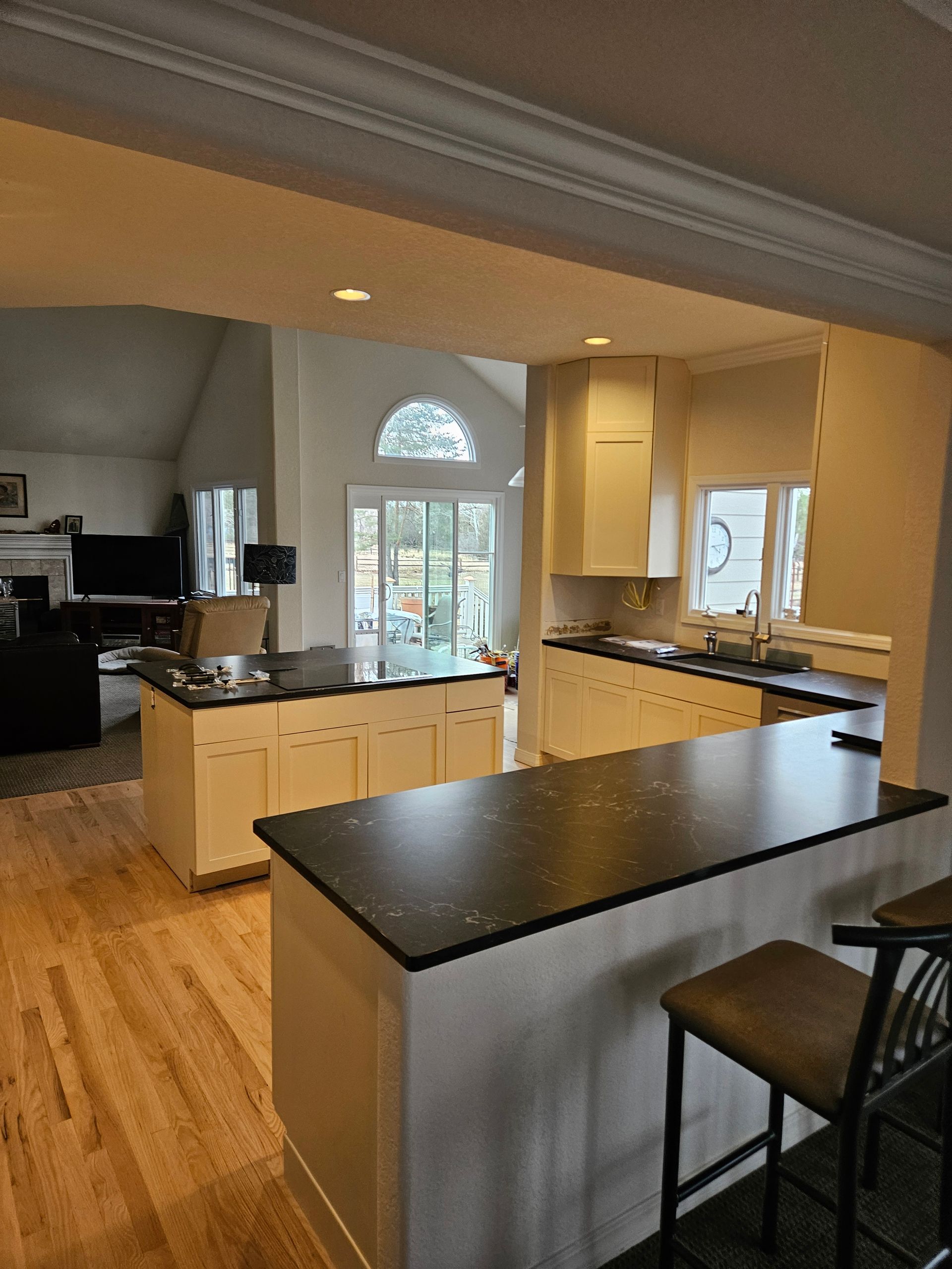 Spacious modern kitchen with black countertops, light cabinets, hardwood floors, and a large island.