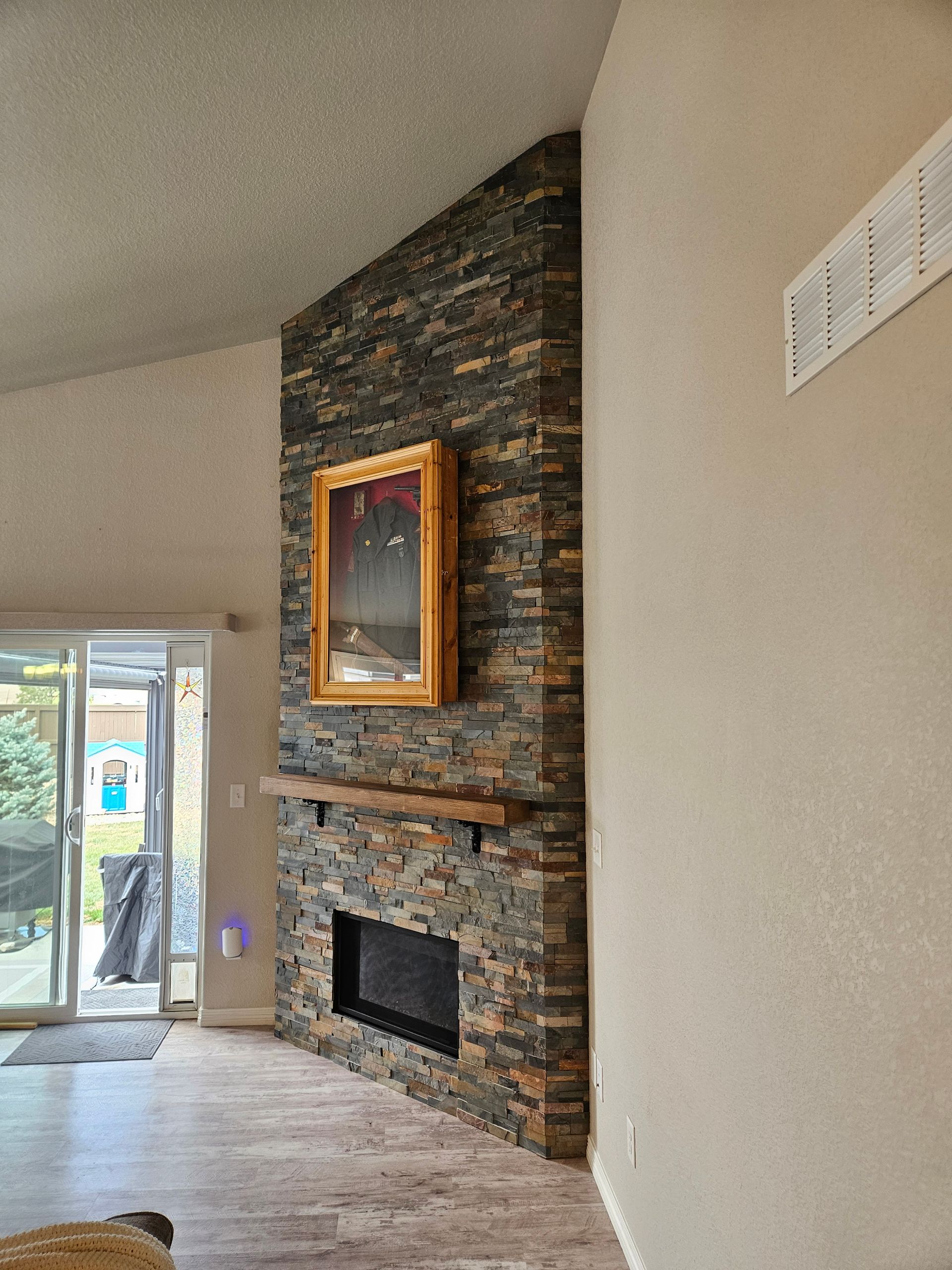 Living room with a stone fireplace, mounted framed art, tall wall, and sliding glass doors.