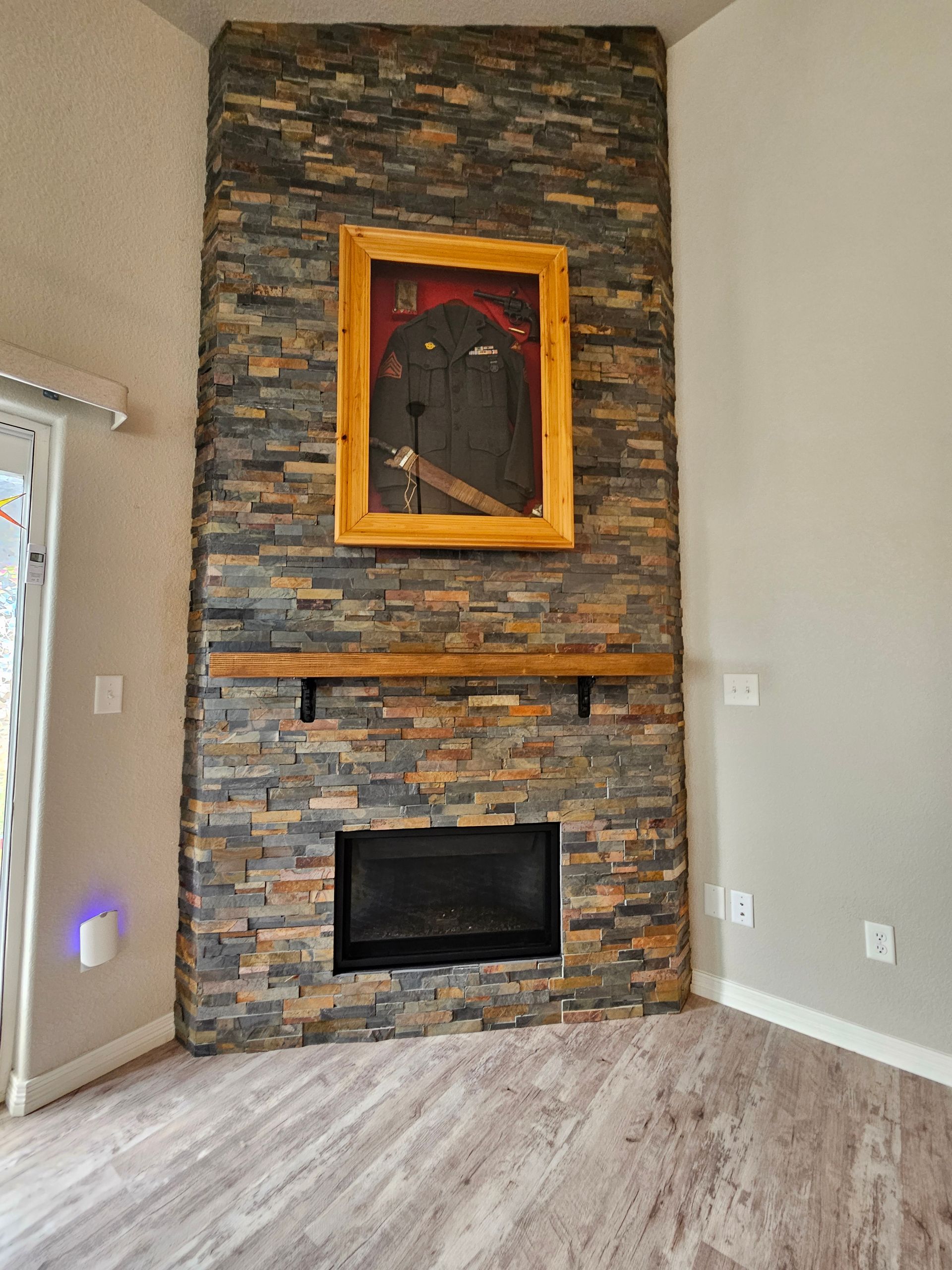 Stone fireplace wall with black firebox and framed niche in a light gray room