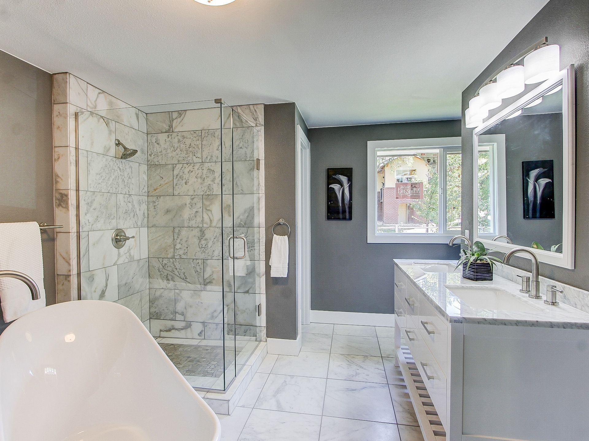 Modern bathroom with glass shower, freestanding tub, double vanity, and gray walls