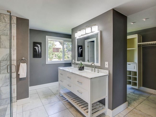 Modern gray bathroom with white vanity, large mirror, tiled floor, and shower area visible