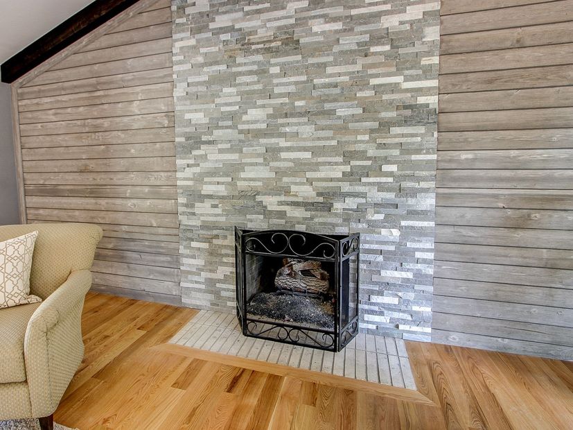 Living room fireplace with stone surround, gray wood-paneled wall, and light wood floor