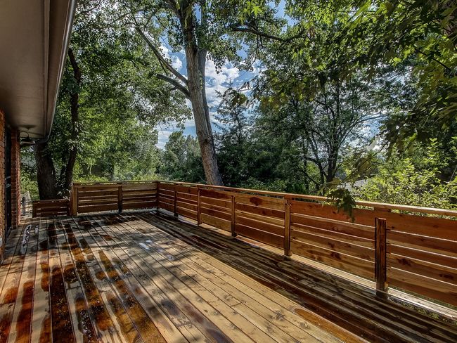 Wooden deck with railing in a wooded backyard, sunlight casting tree shadows across the floor.