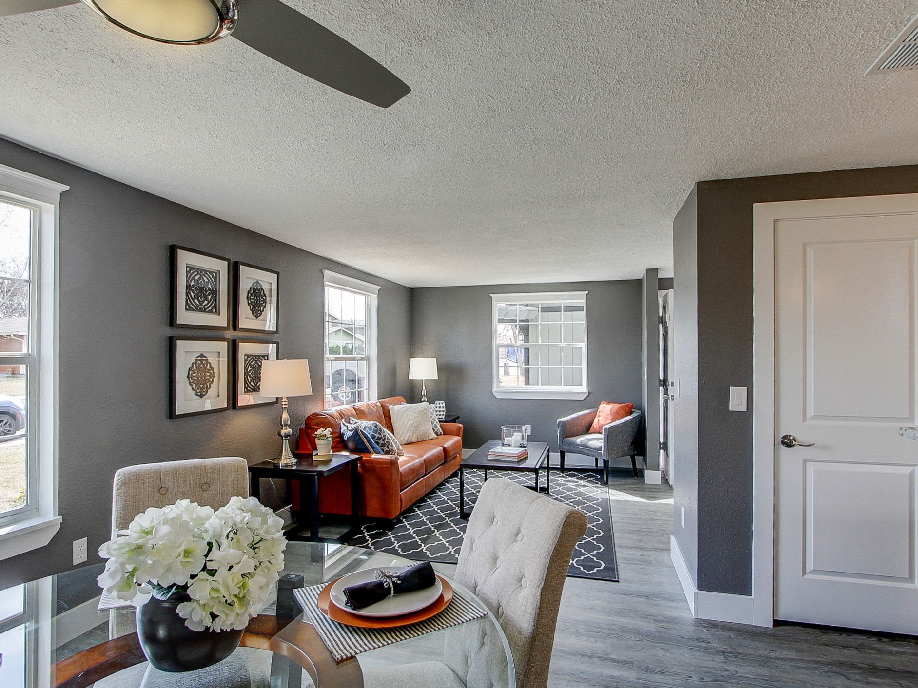 Bright living room with gray walls, orange sofa, white chair, dining table, and ceiling fan.
