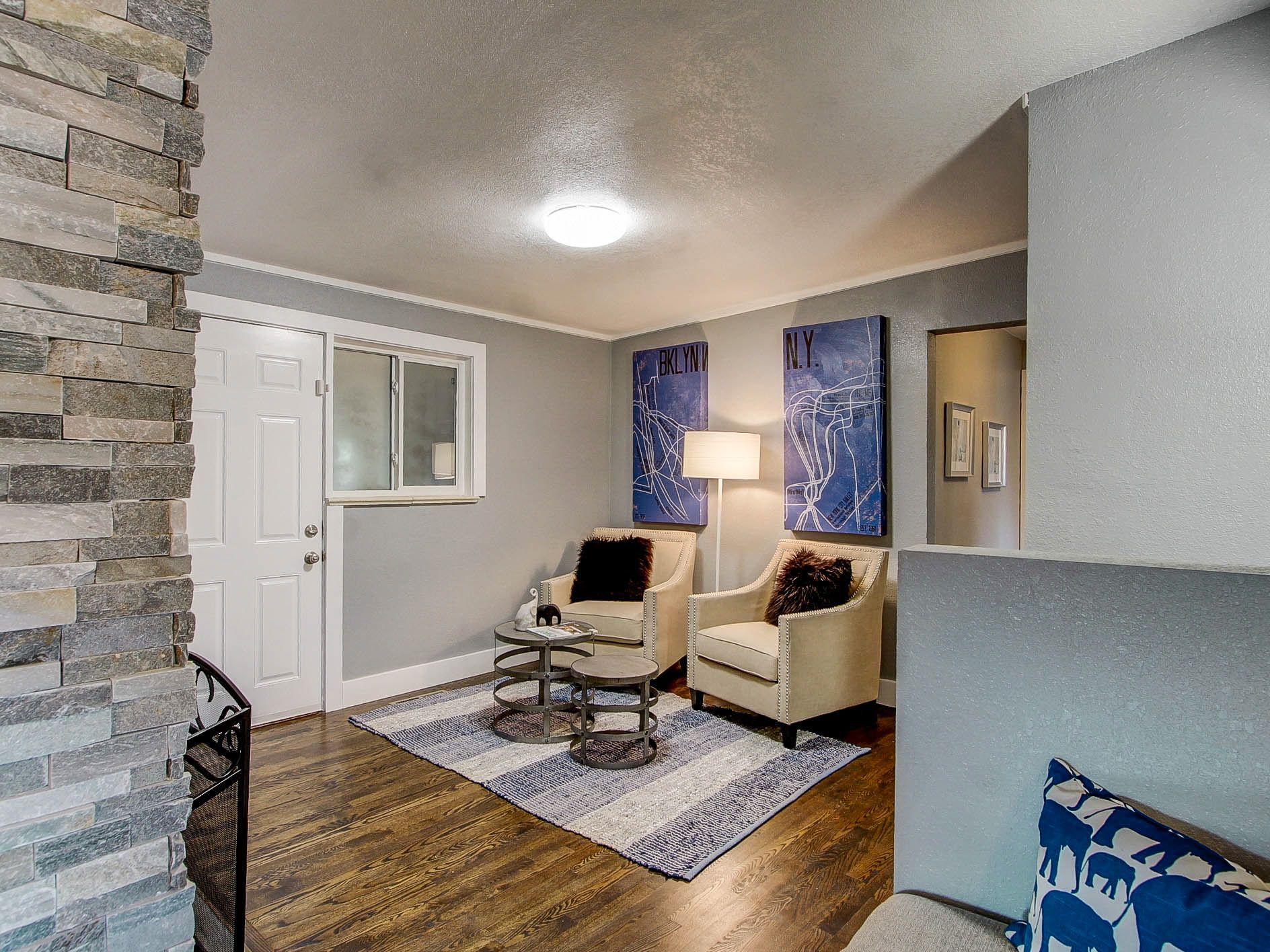 Cozy living room with beige chair, lamp, rug, stone fireplace, and front door