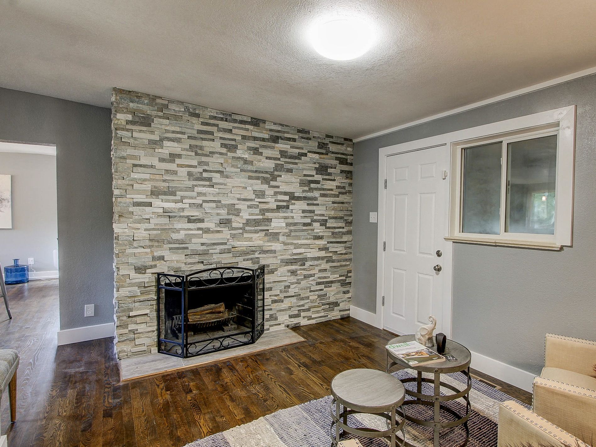 Living room with stone fireplace, gray walls, white door, and hardwood floors
