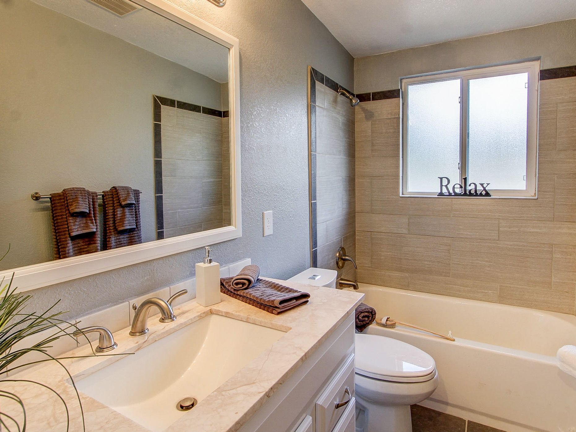 Bright bathroom with vanity, large mirror, bathtub, and a “Relax” sign on the window.