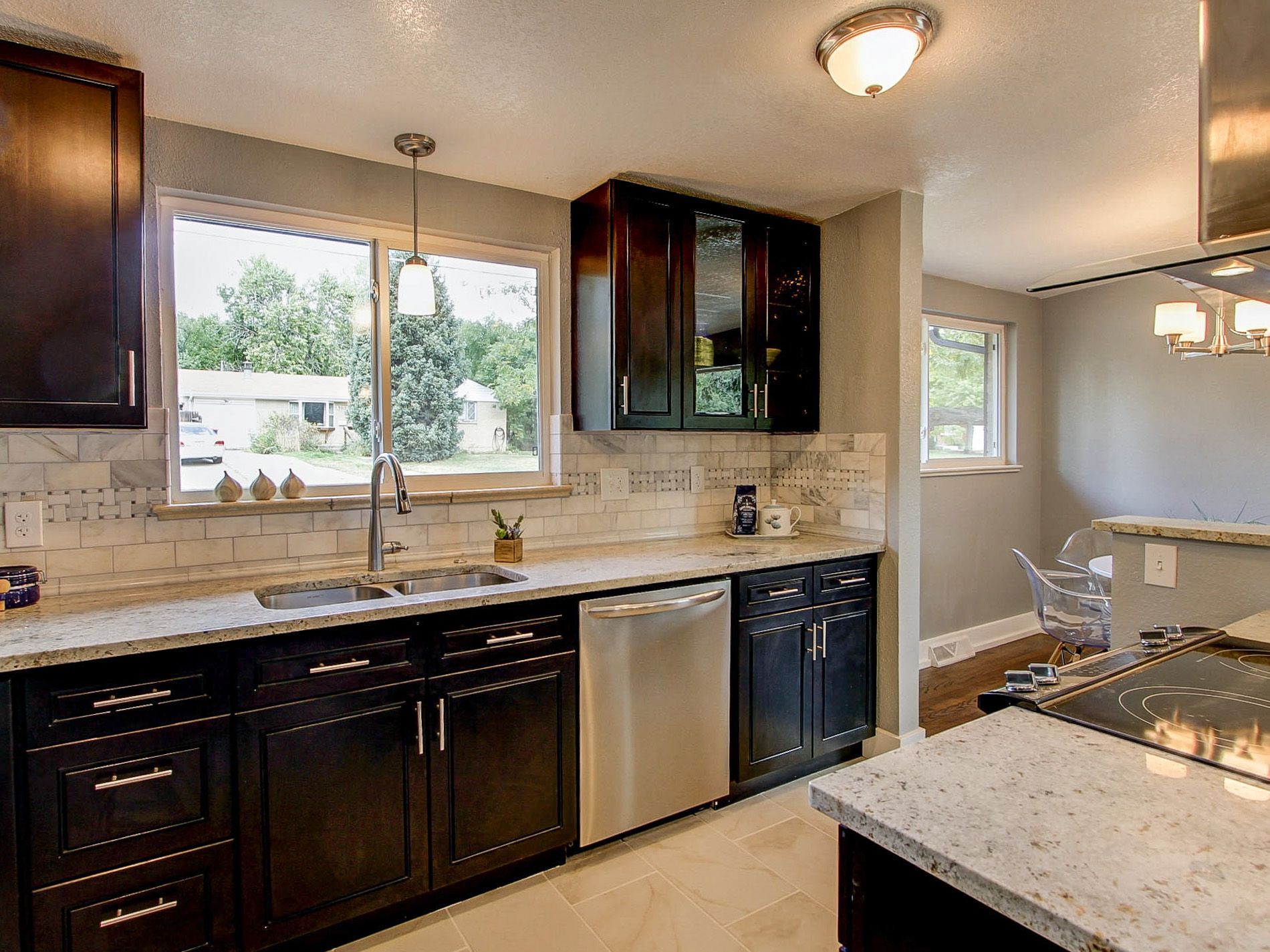 Modern kitchen with dark cabinets, granite counters, stainless dishwasher, and a window over the sink.