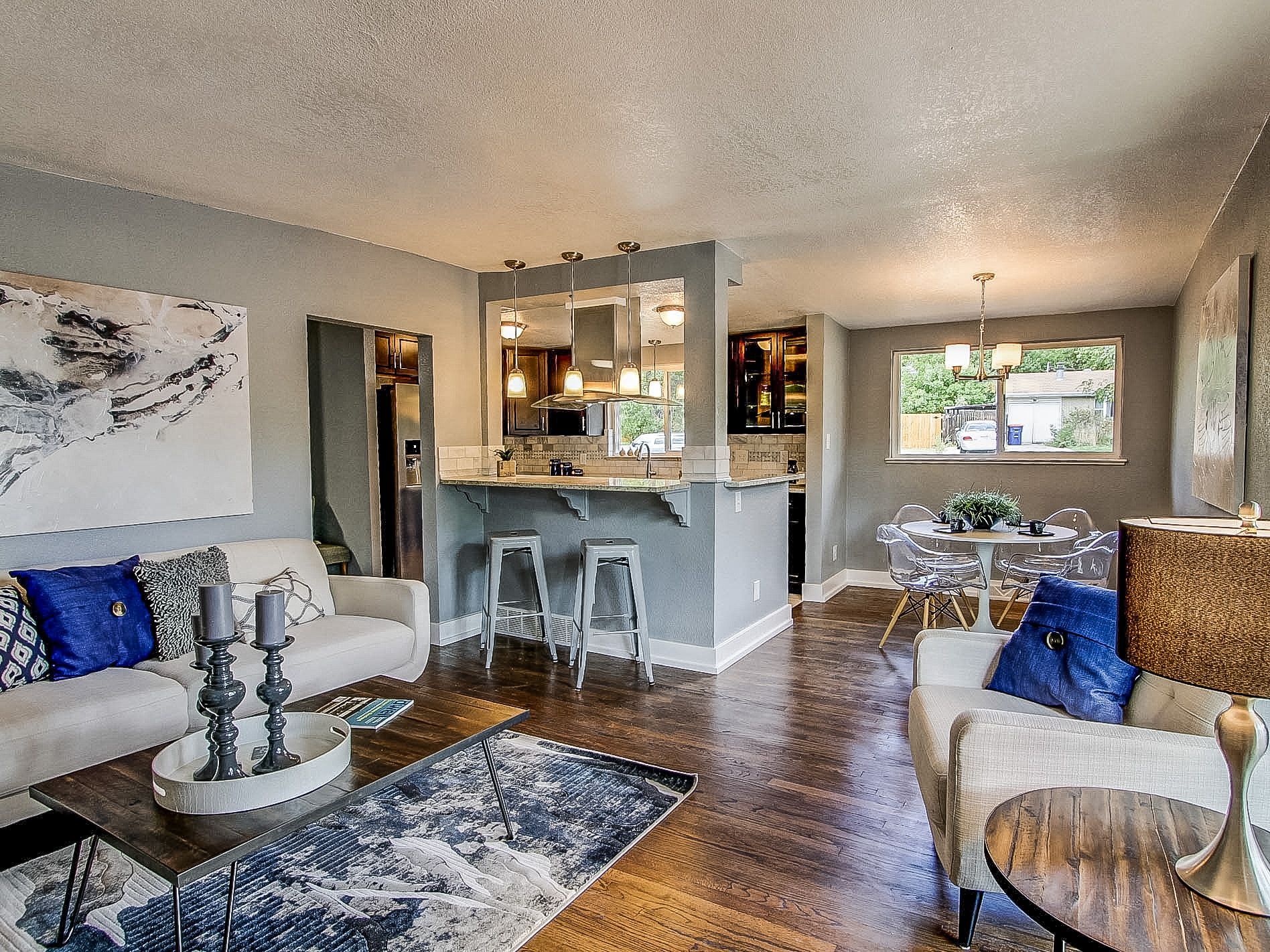Bright modern living room with gray sofas, blue accents, wood floors, and a kitchen pass-through.