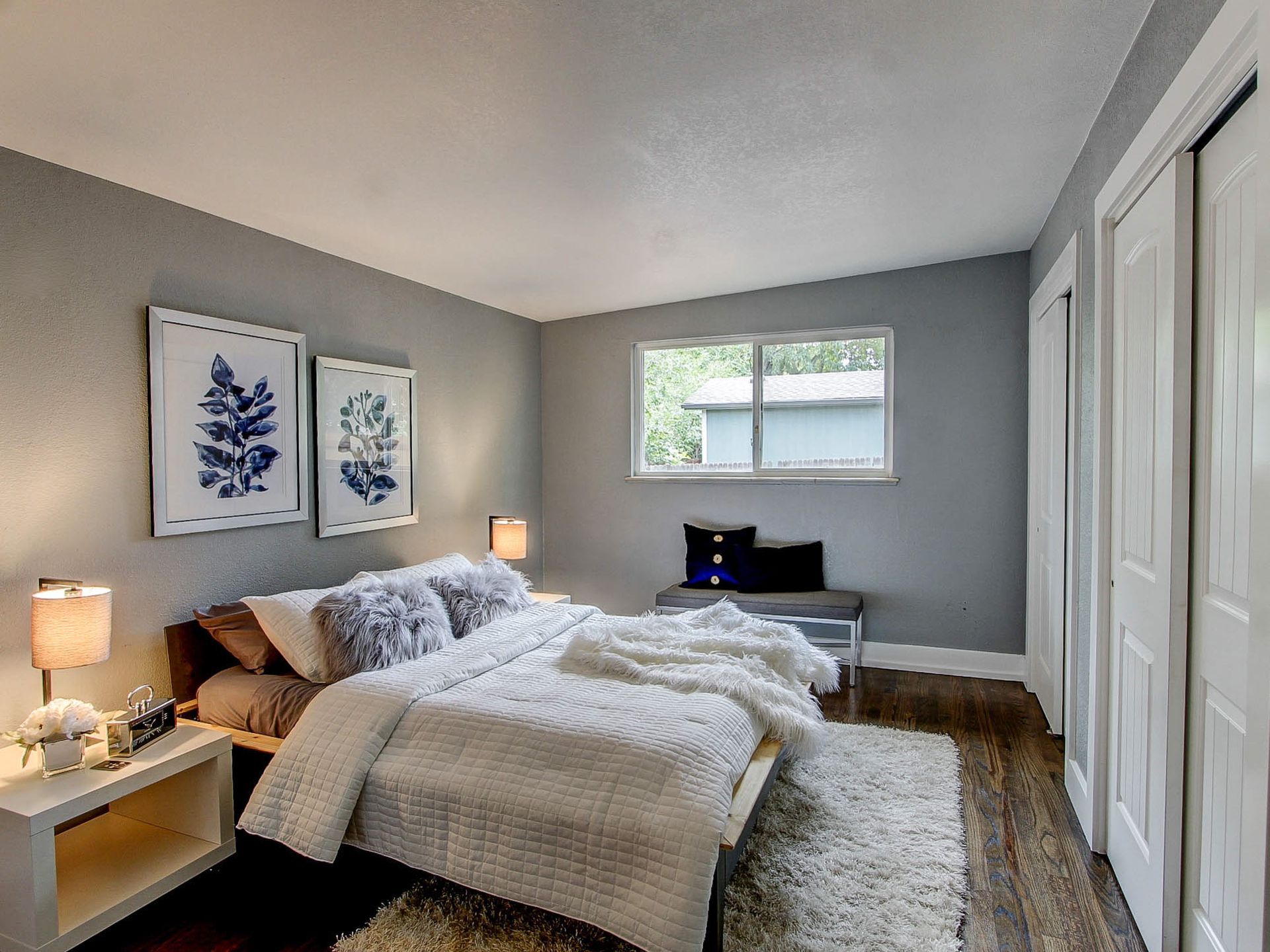 Bright bedroom with a bed, nightstand lamps, window, desk, and white closet doors