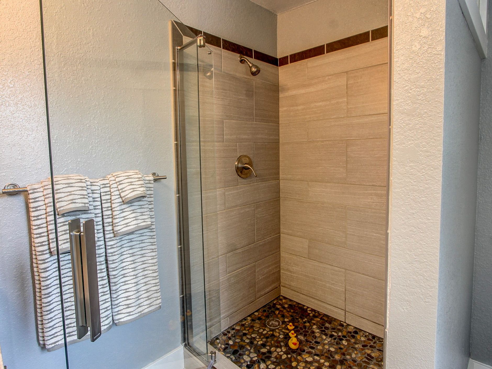 Glass walk-in shower with beige tile walls, chrome fixtures, and pebble mosaic floor.