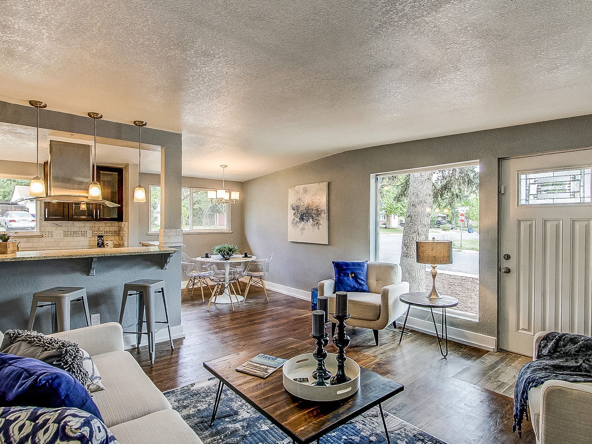 Bright living room with blue chairs, glass coffee table, fireplace, and large window view