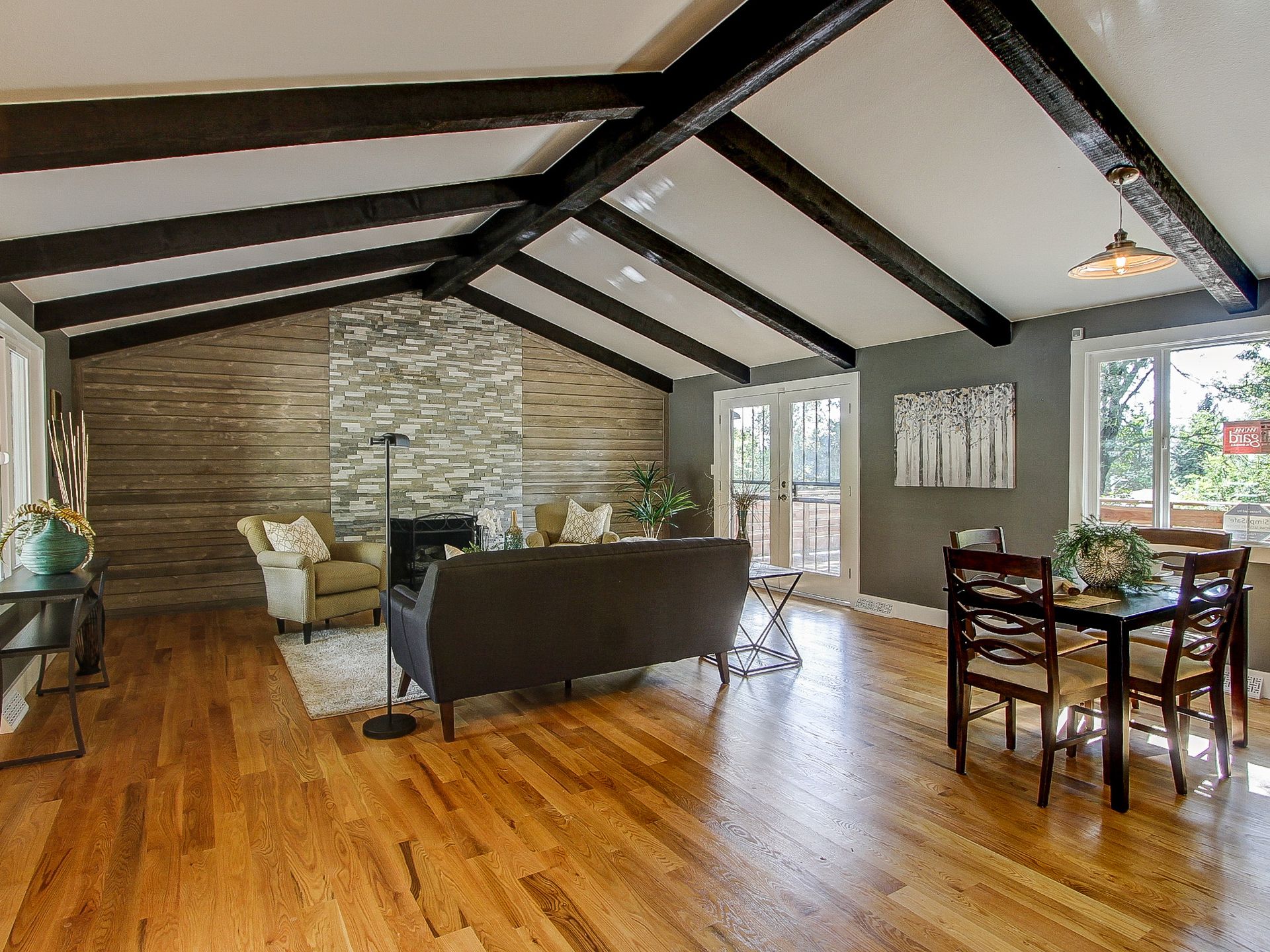 Open living room with wood floors, vaulted ceiling, sofa, chairs, and dining table by windows