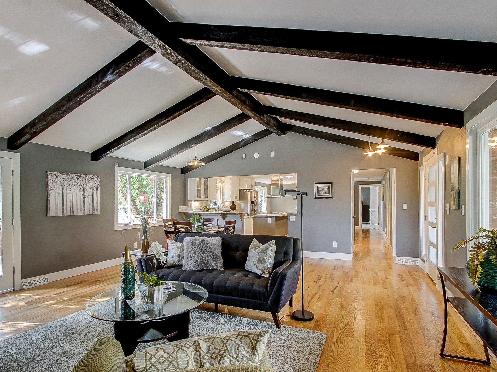 Spacious living room with vaulted ceiling, exposed beams, hardwood floors, and dark leather seating.