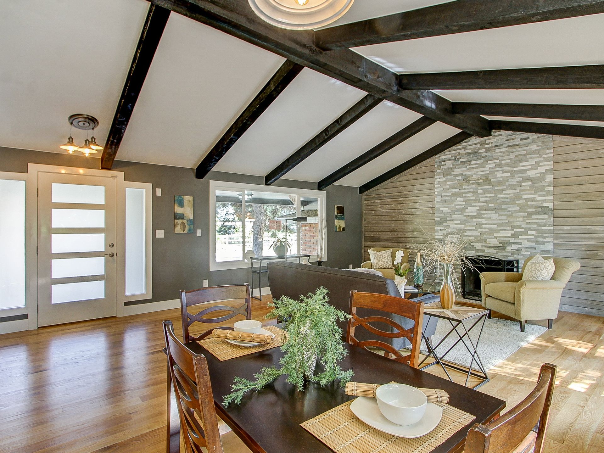 Open living room with vaulted wood-beam ceiling, stone wall, and dining table in foreground