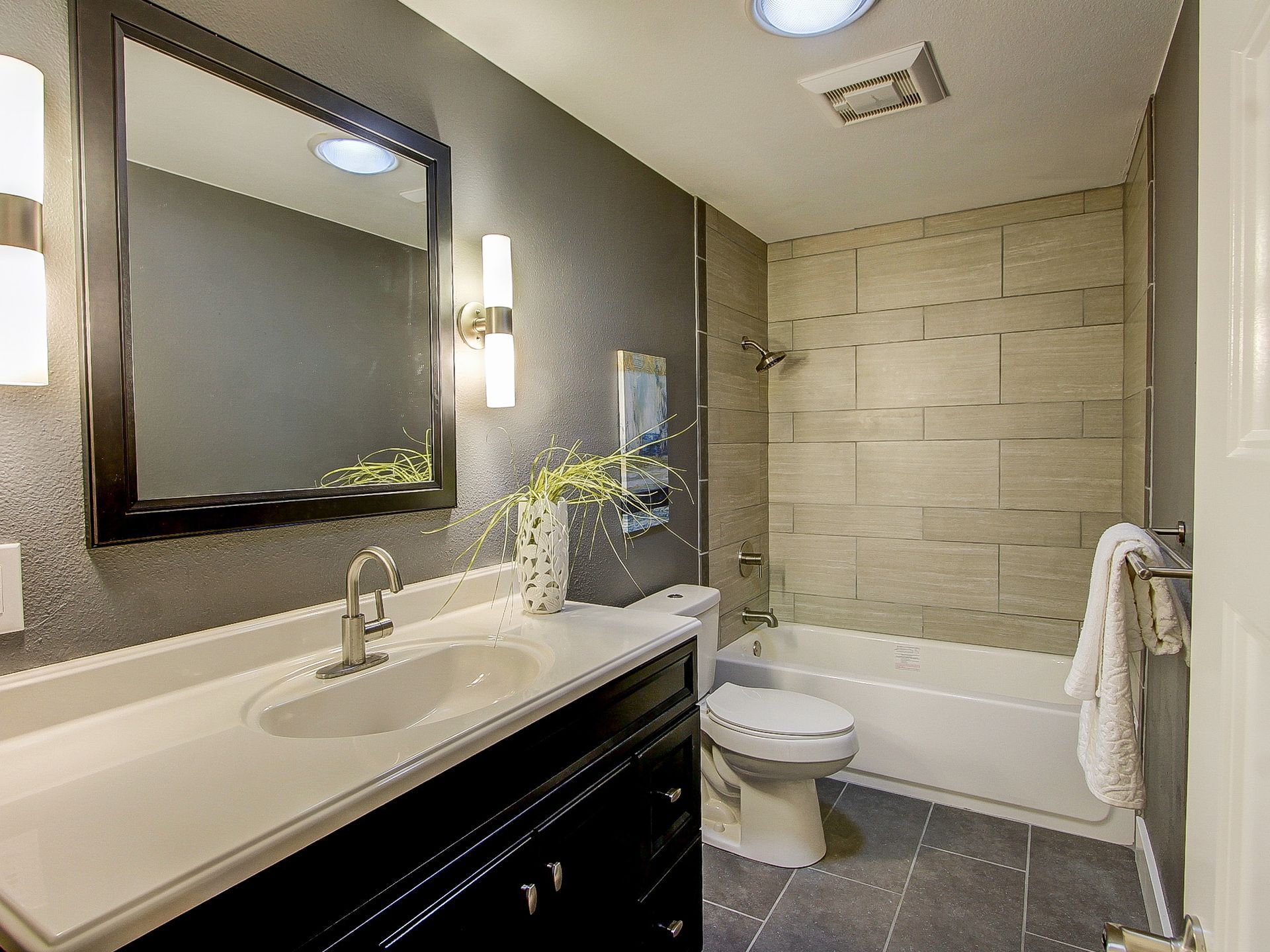 Modern bathroom with vanity, mirror, toilet, bathtub, and beige tile walls