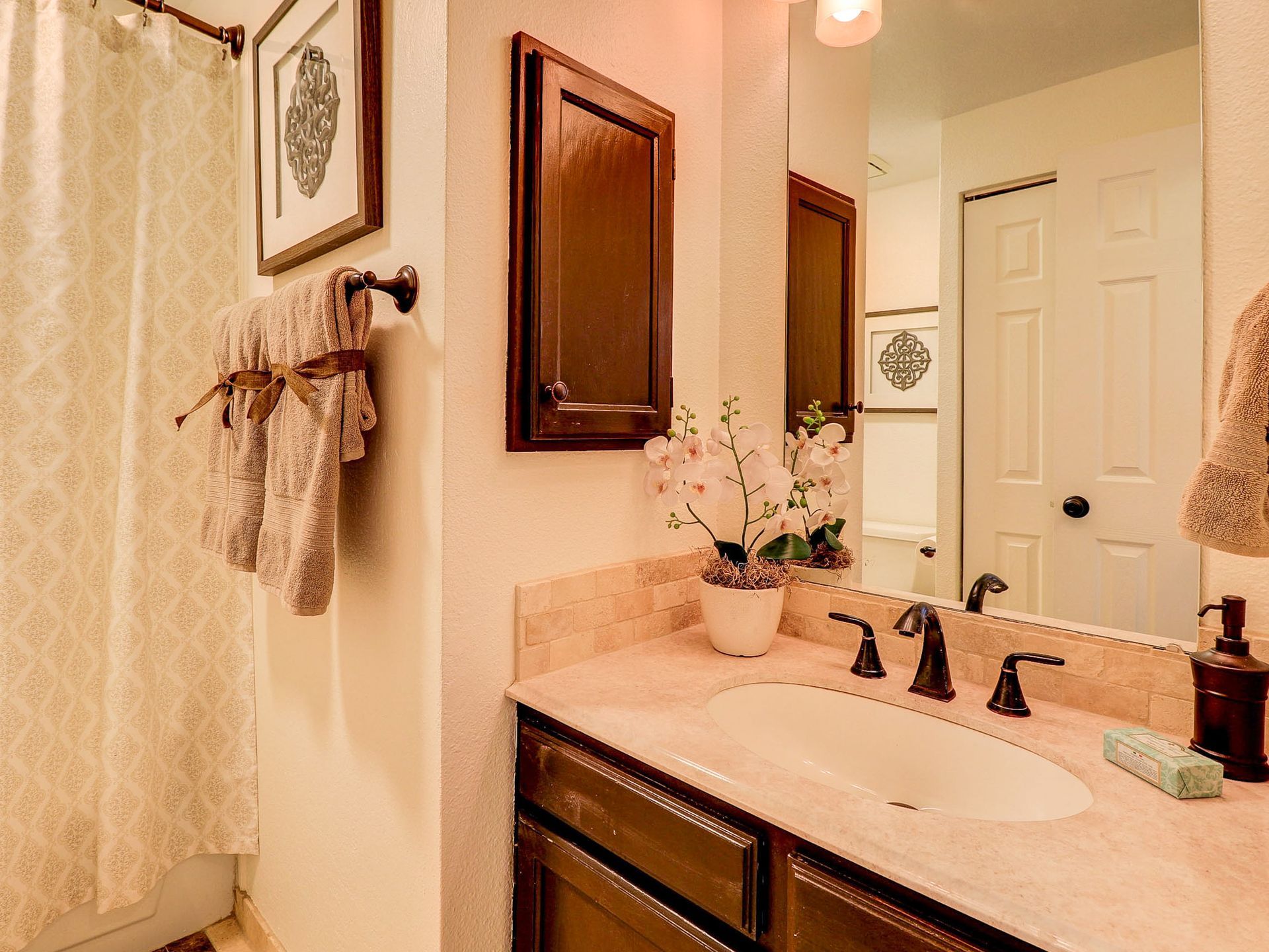 Bathroom vanity with sink, mirror, black faucet, and floral decor in a beige room