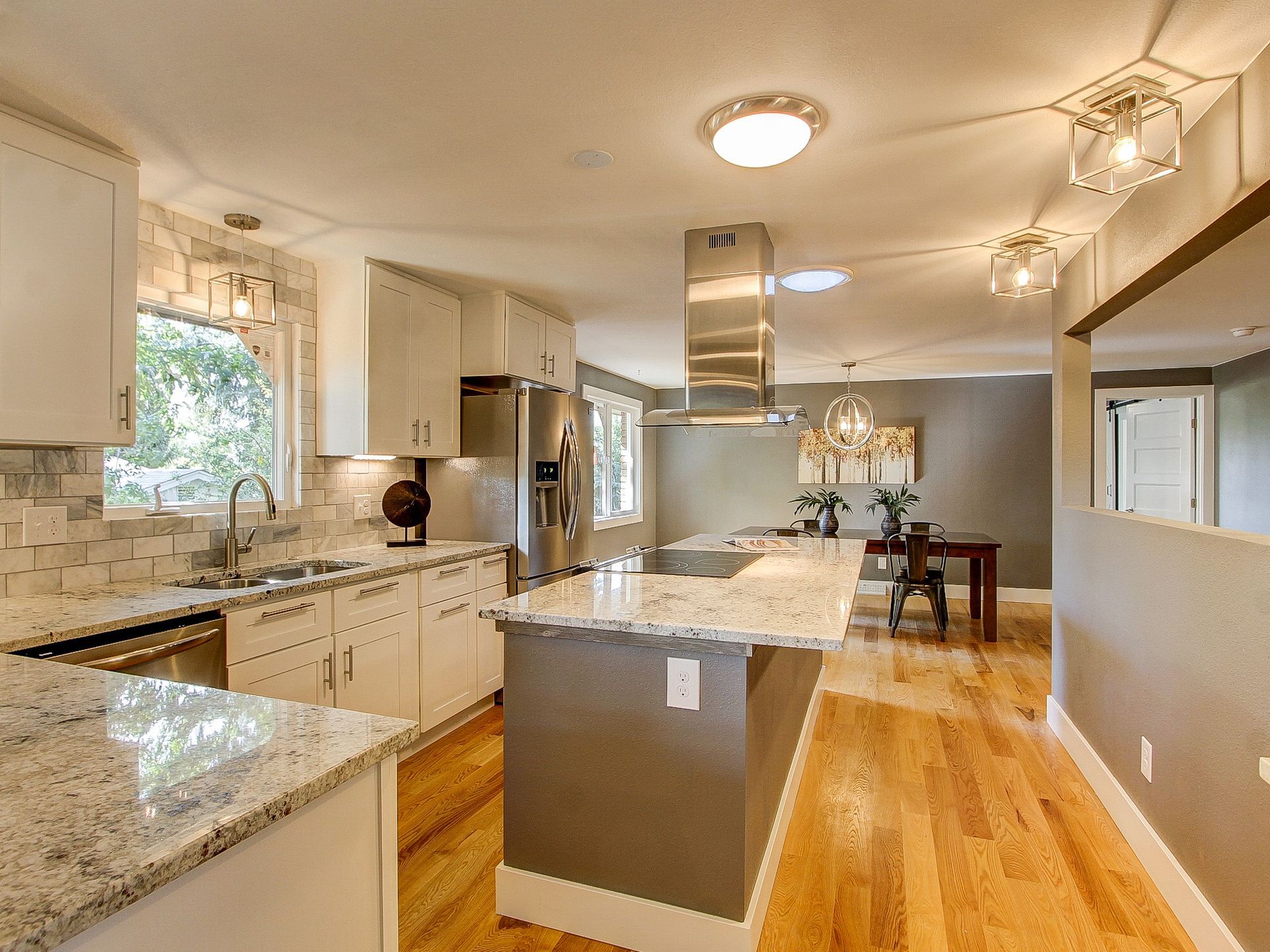 Bright modern kitchen with granite island, white cabinets, wood floors, and stainless steel range hood