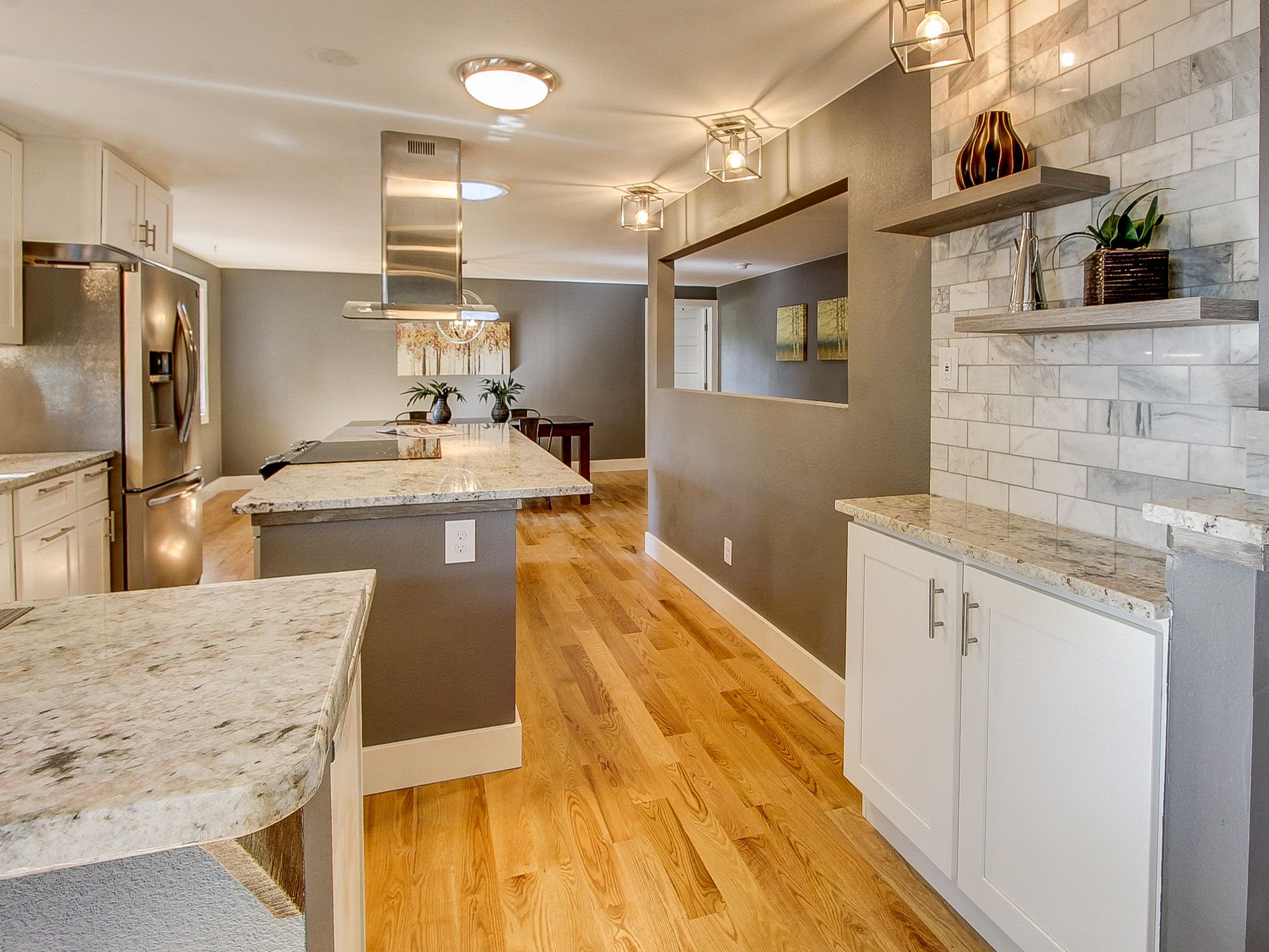 Modern kitchen with white cabinets, granite island, hardwood floors, and gray walls with open shelving