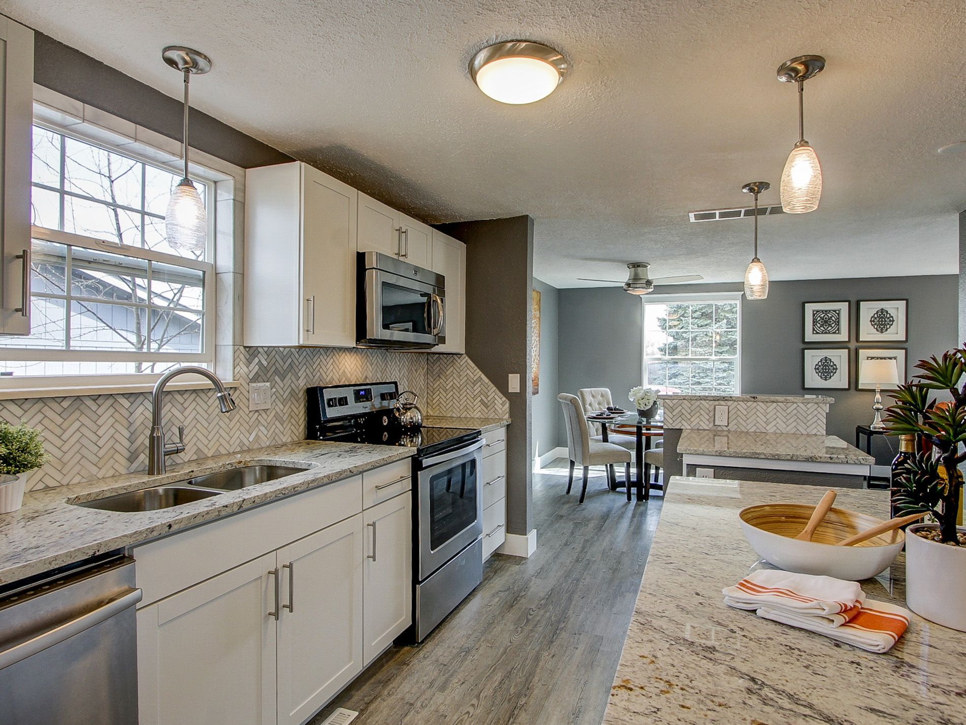 Bright modern kitchen with white cabinets, granite counters, stainless appliances, and pendant lights opening to dining area