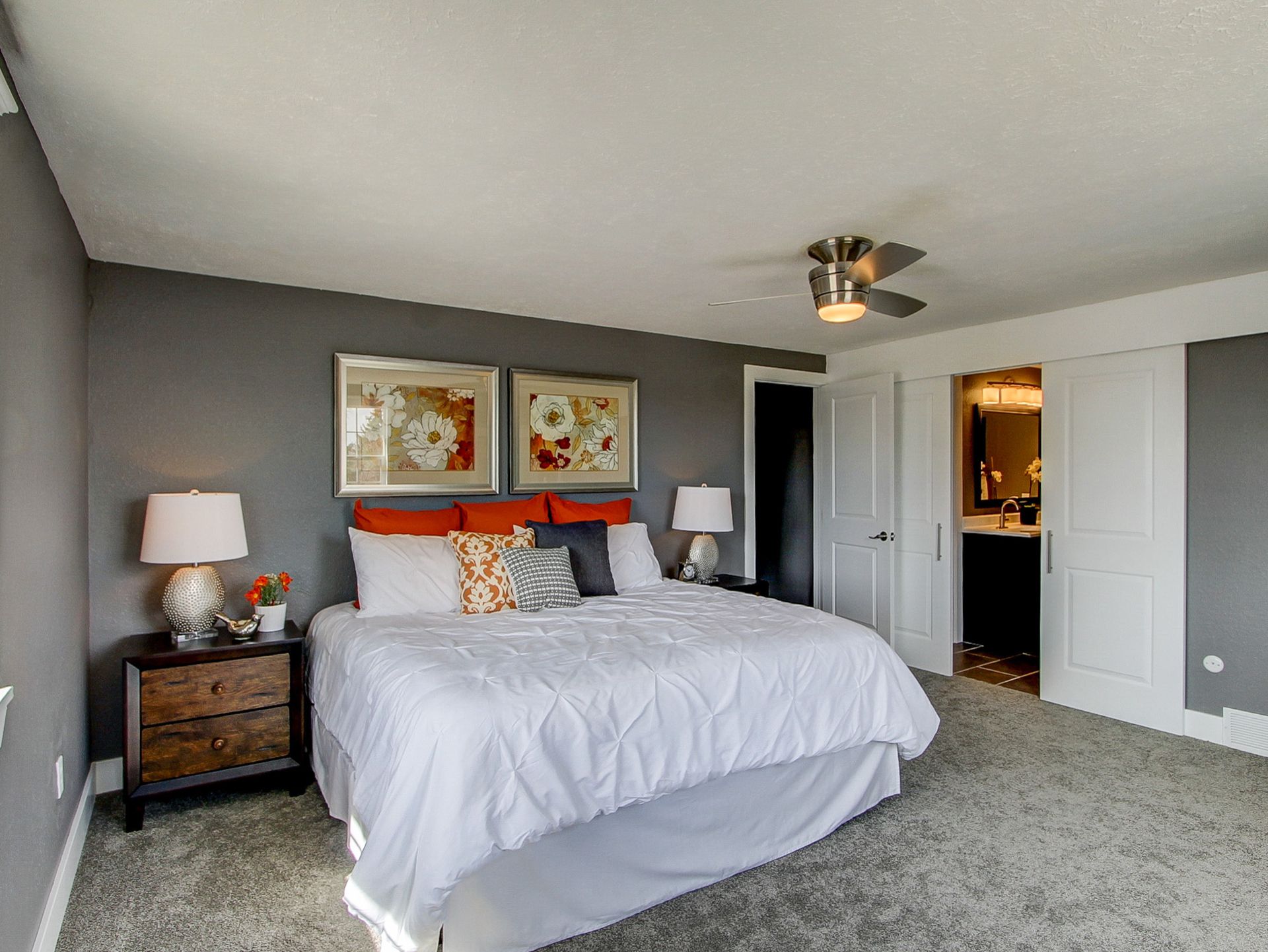 Gray bedroom with a bed, nightstands, lamps, framed art, and a ceiling fan