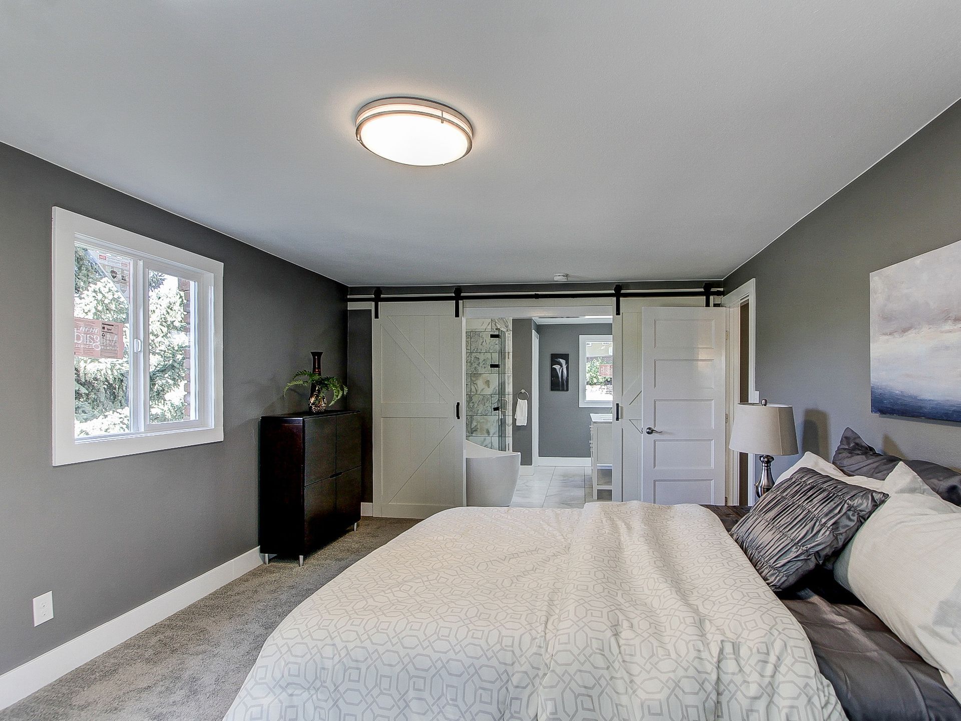 Bright gray bedroom with a bed, window, dresser, and mirror closet doors