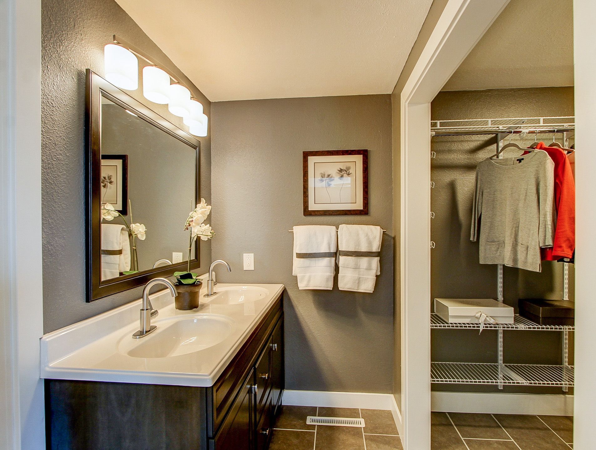 Bathroom with vanity and mirror on the left, and an open closet with hanging clothes on the right.