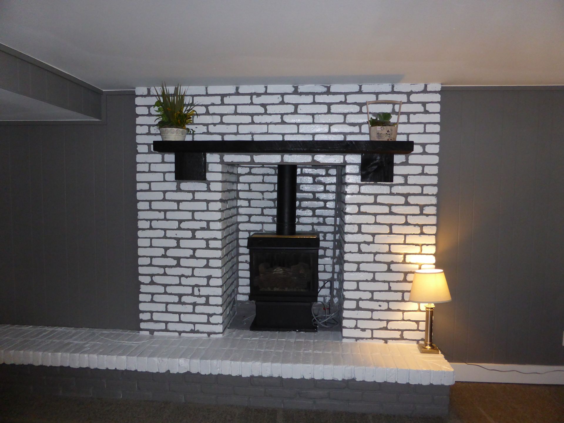 Living room with white brick fireplace, dark gray walls, potted plants, and a lit floor lamp