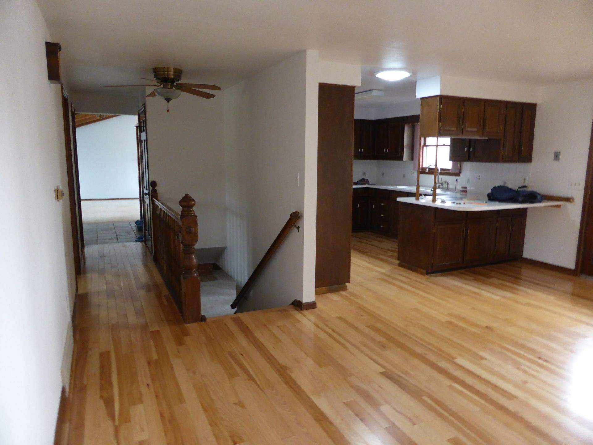 Open living room with hardwood floors, staircase, and kitchen area in the back.