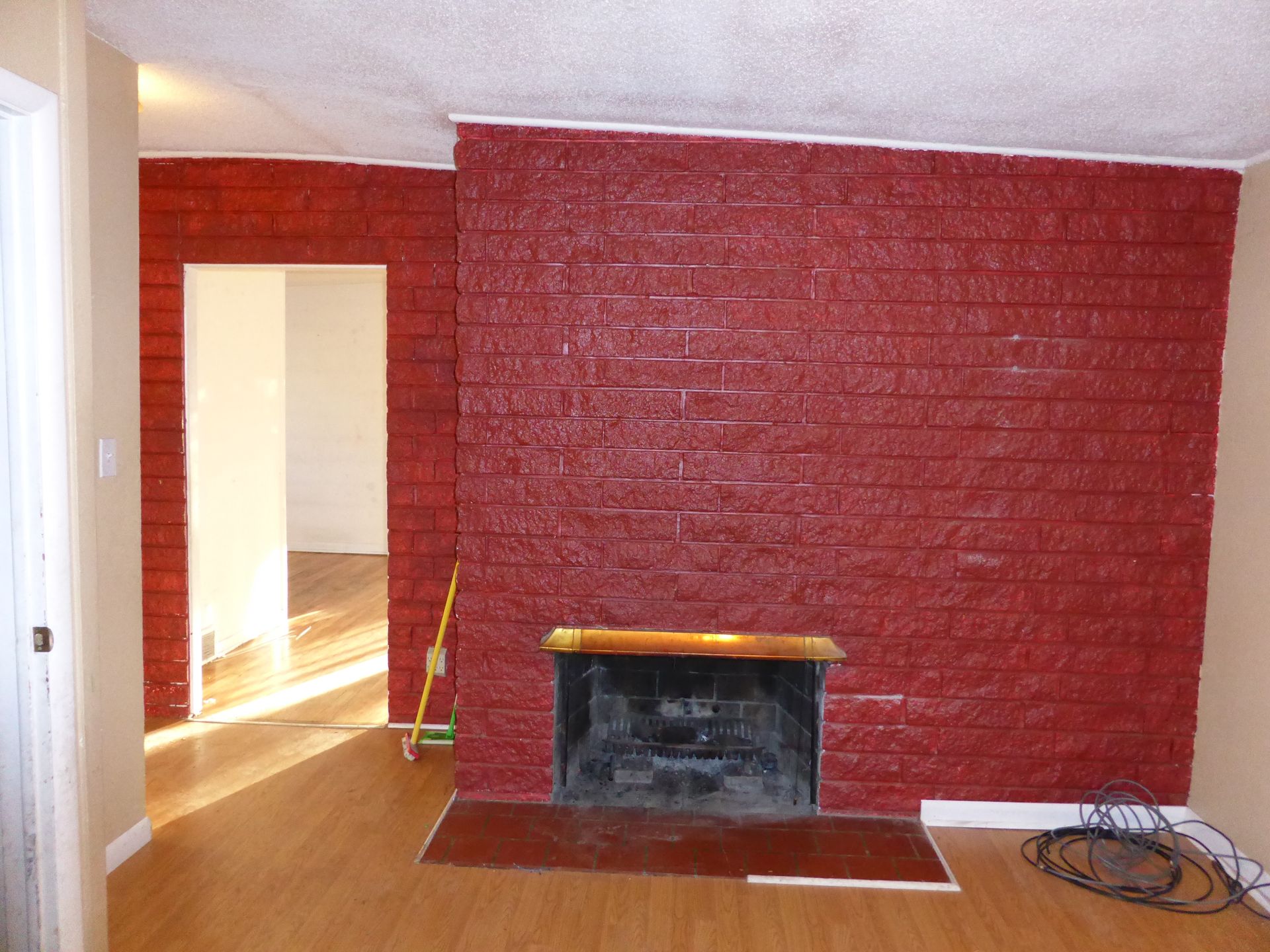 Empty room with red brick fireplace, white walls, and hardwood floor