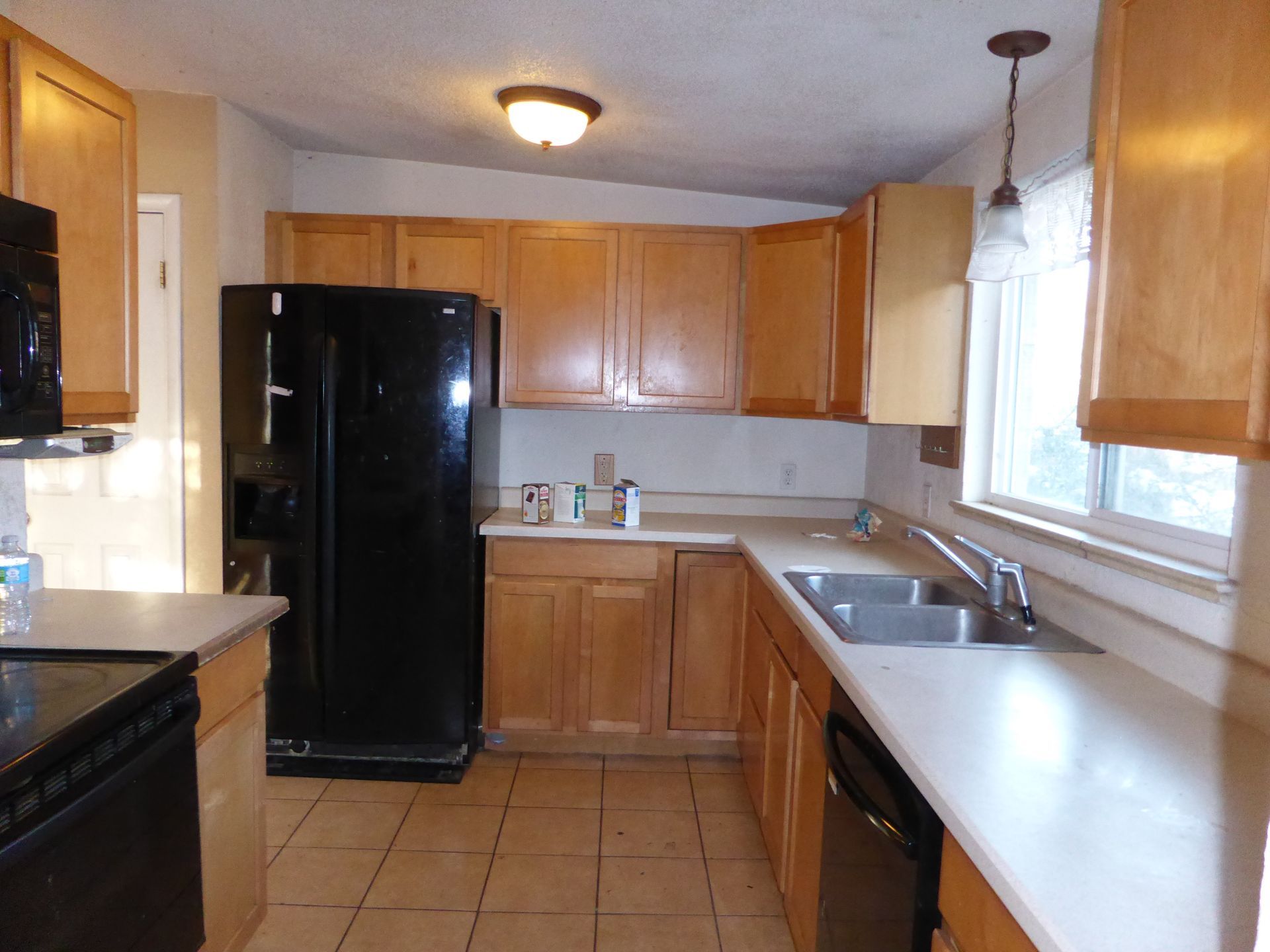 Compact kitchen with wood cabinets, black refrigerator, white counters, and tiled floor.