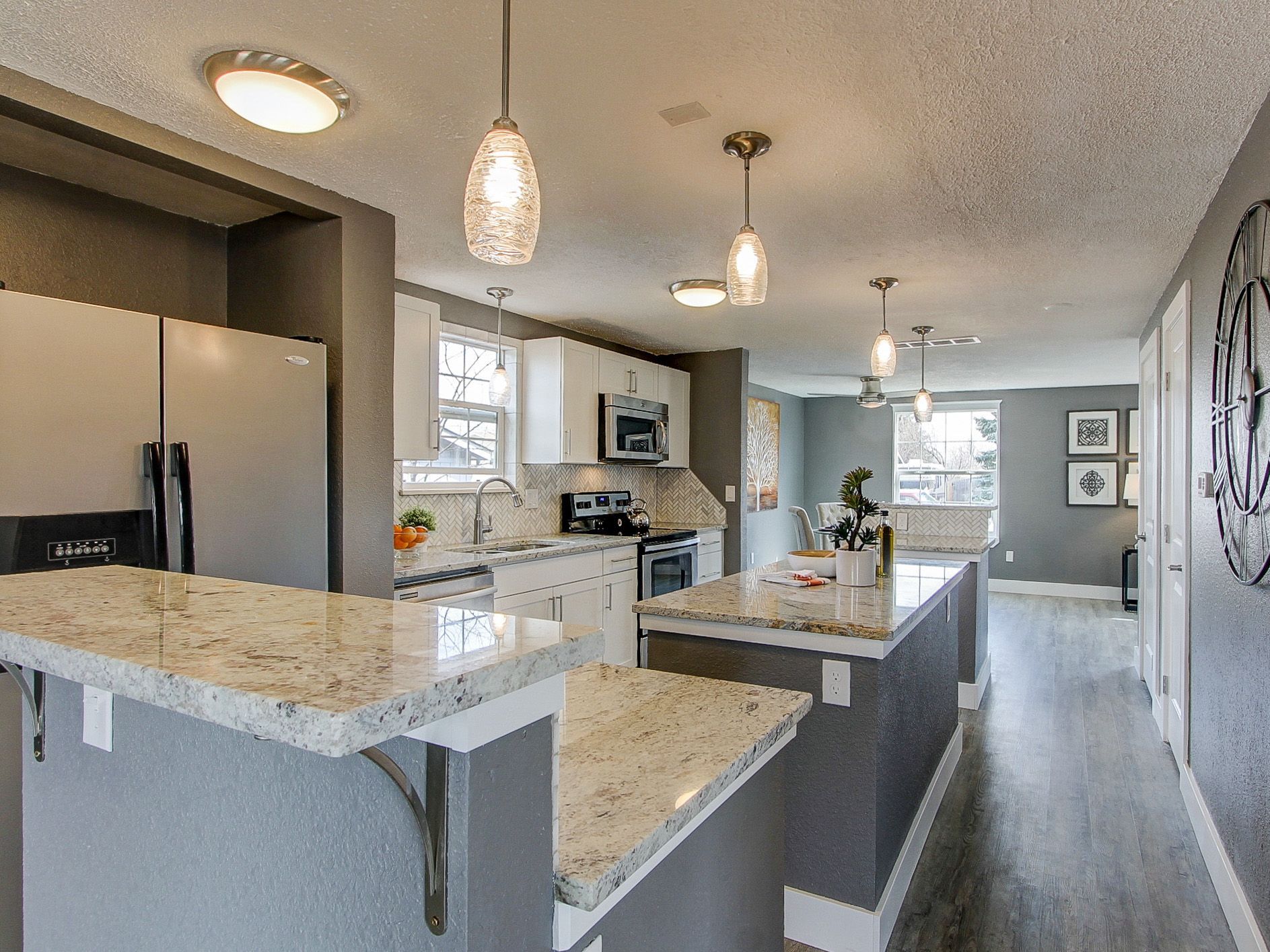 Modern kitchen with granite island, pendant lights, gray cabinets, and open living area