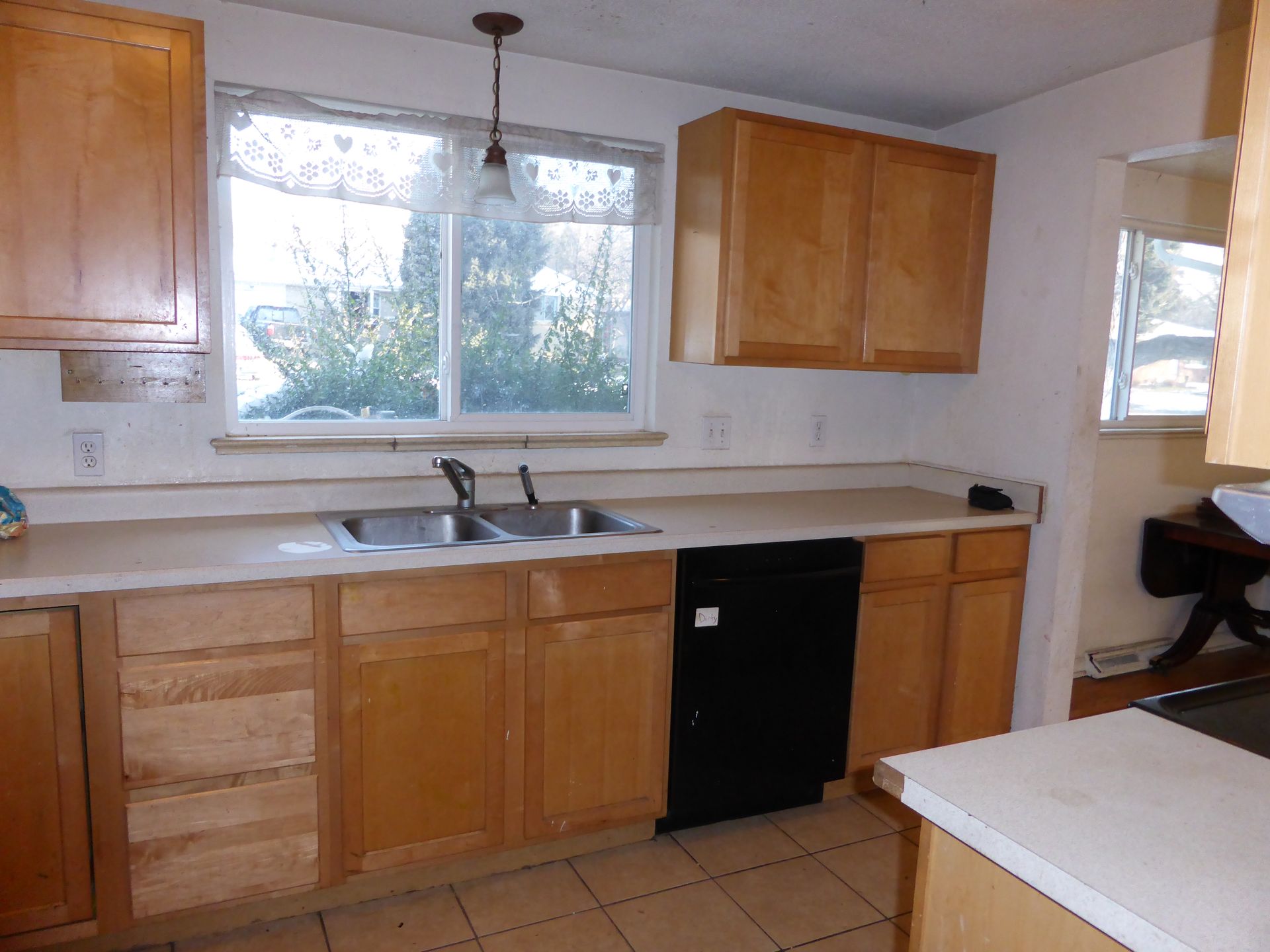 Kitchen with wood cabinets, white counters, sink under a window, and a black dishwasher.