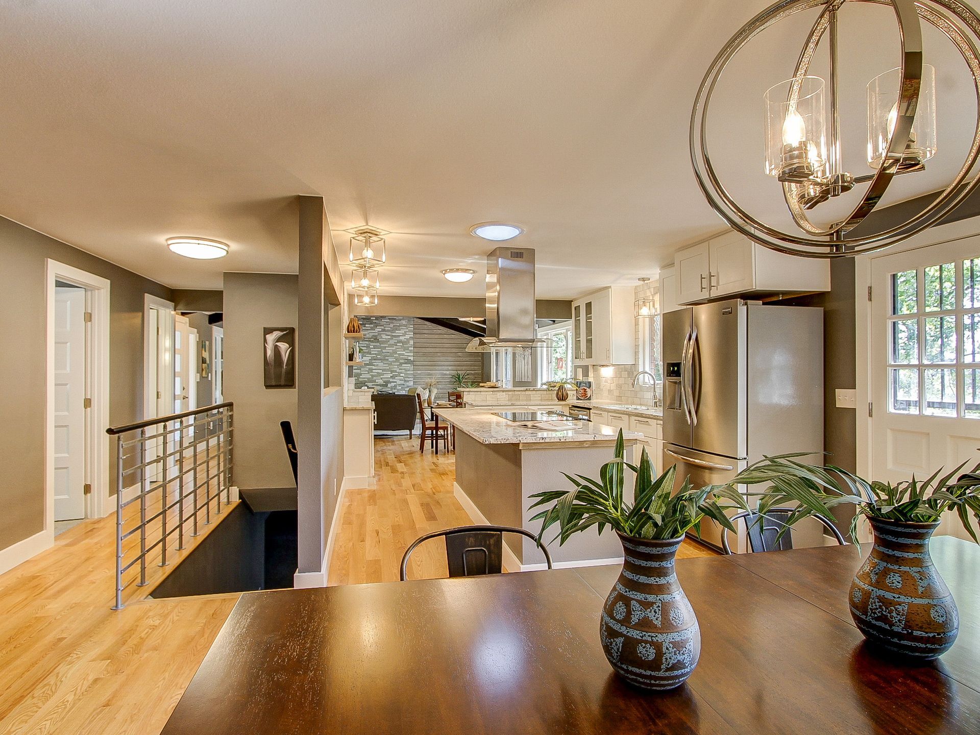 Bright open kitchen and dining area with wooden floors, stainless steel appliances, and a table with vases of plants