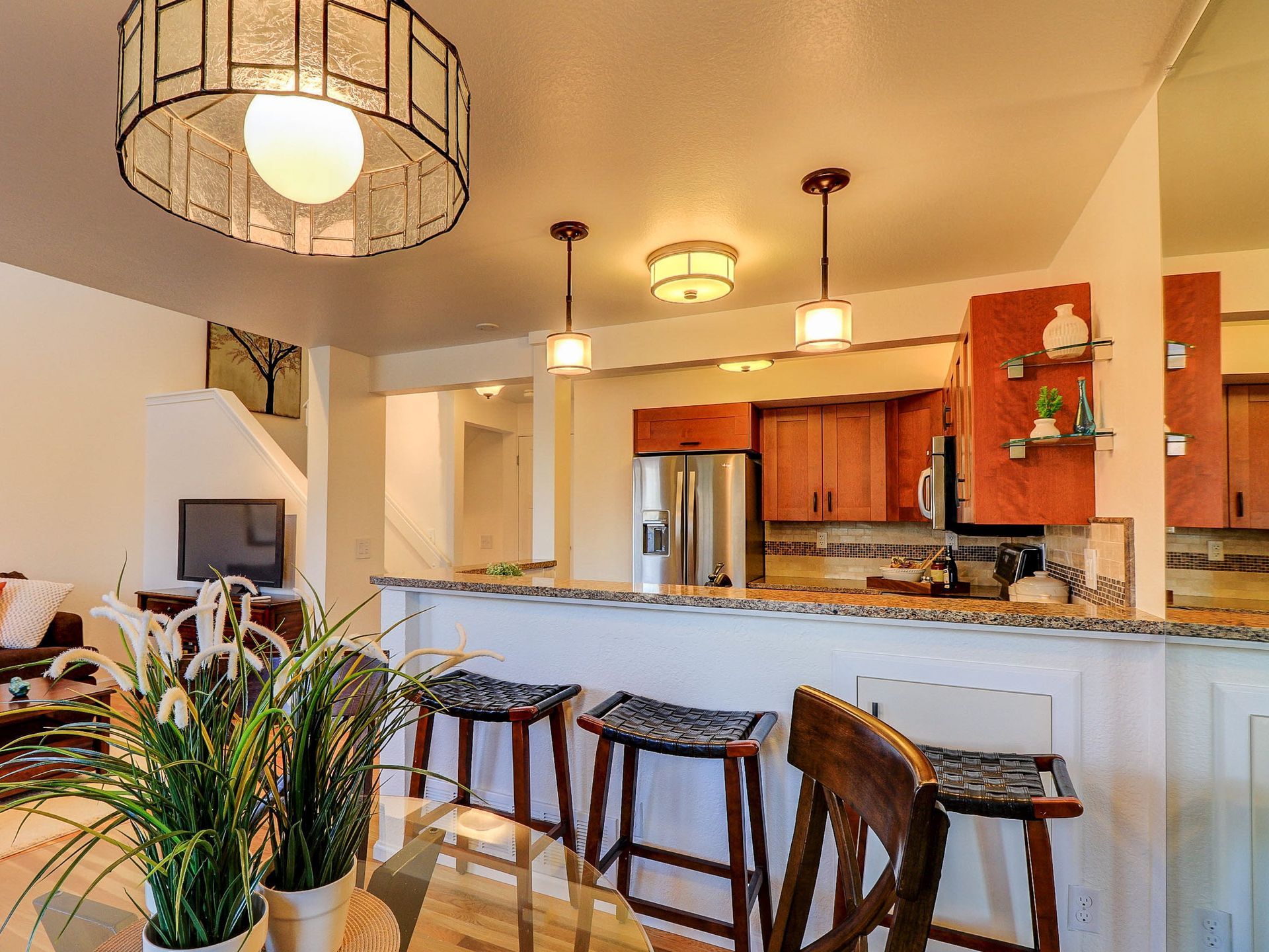 Bright open kitchen with white island, bar stools, pendant lights, stainless fridge, and orange cabinets
